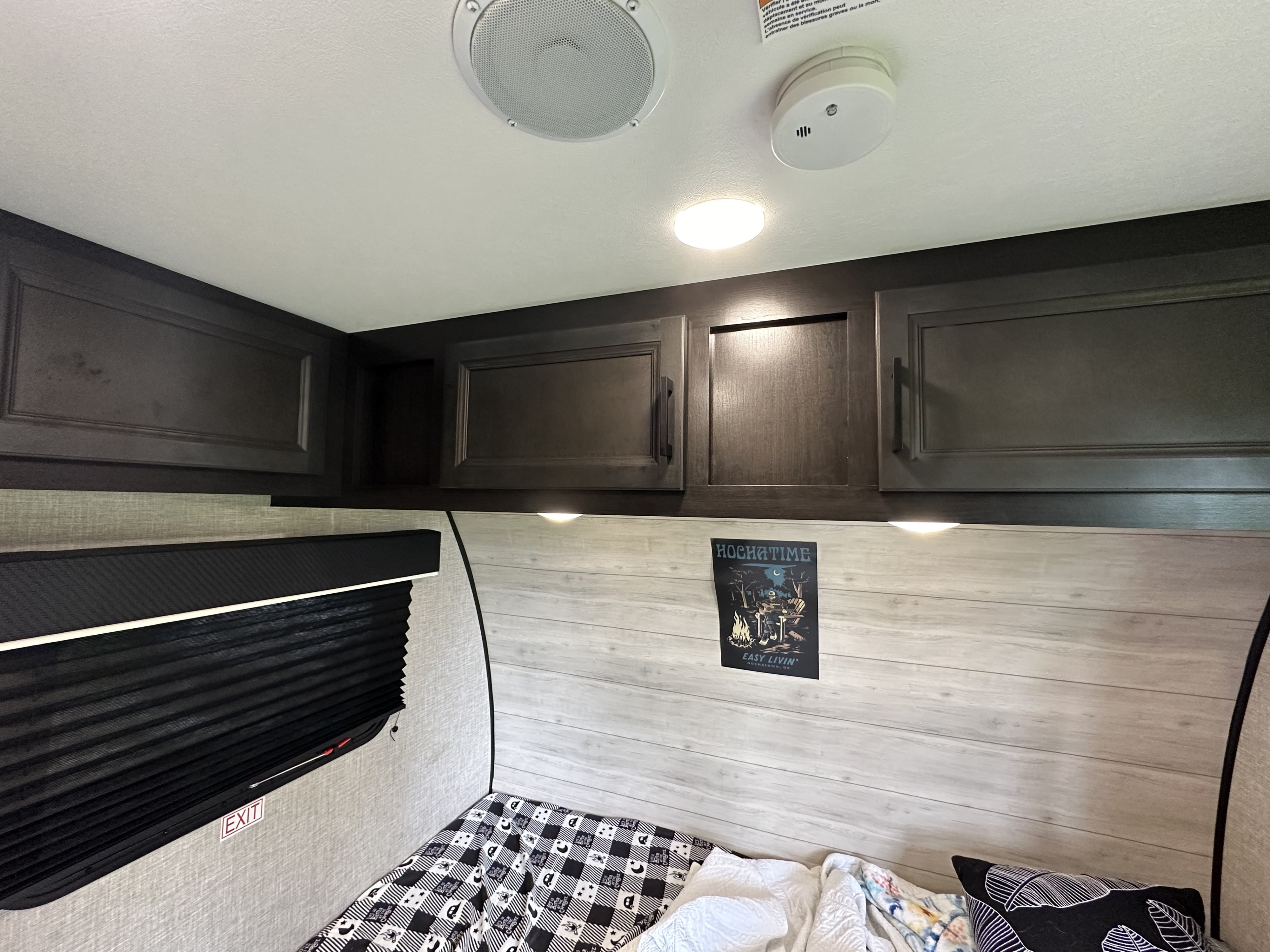 Cozy RV rental bedroom showing overhead cabinets, bed, ceiling light, speaker, and window shade for travel.. Jayco Jay Flight SLX 2024