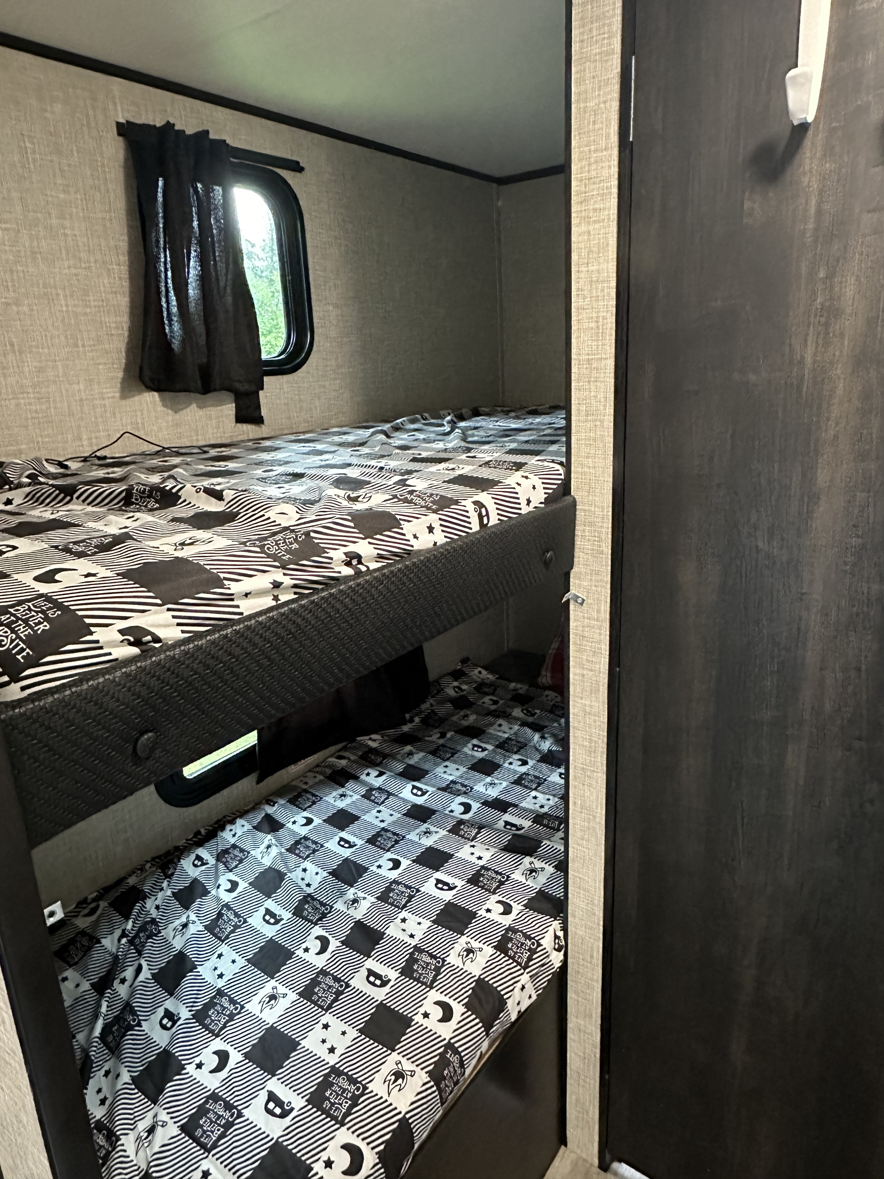 Inside an RV rental: black & white patterned bunk beds with "Life is Better at the Campsite" sheets and a window.. Jayco Jay Flight SLX 2024