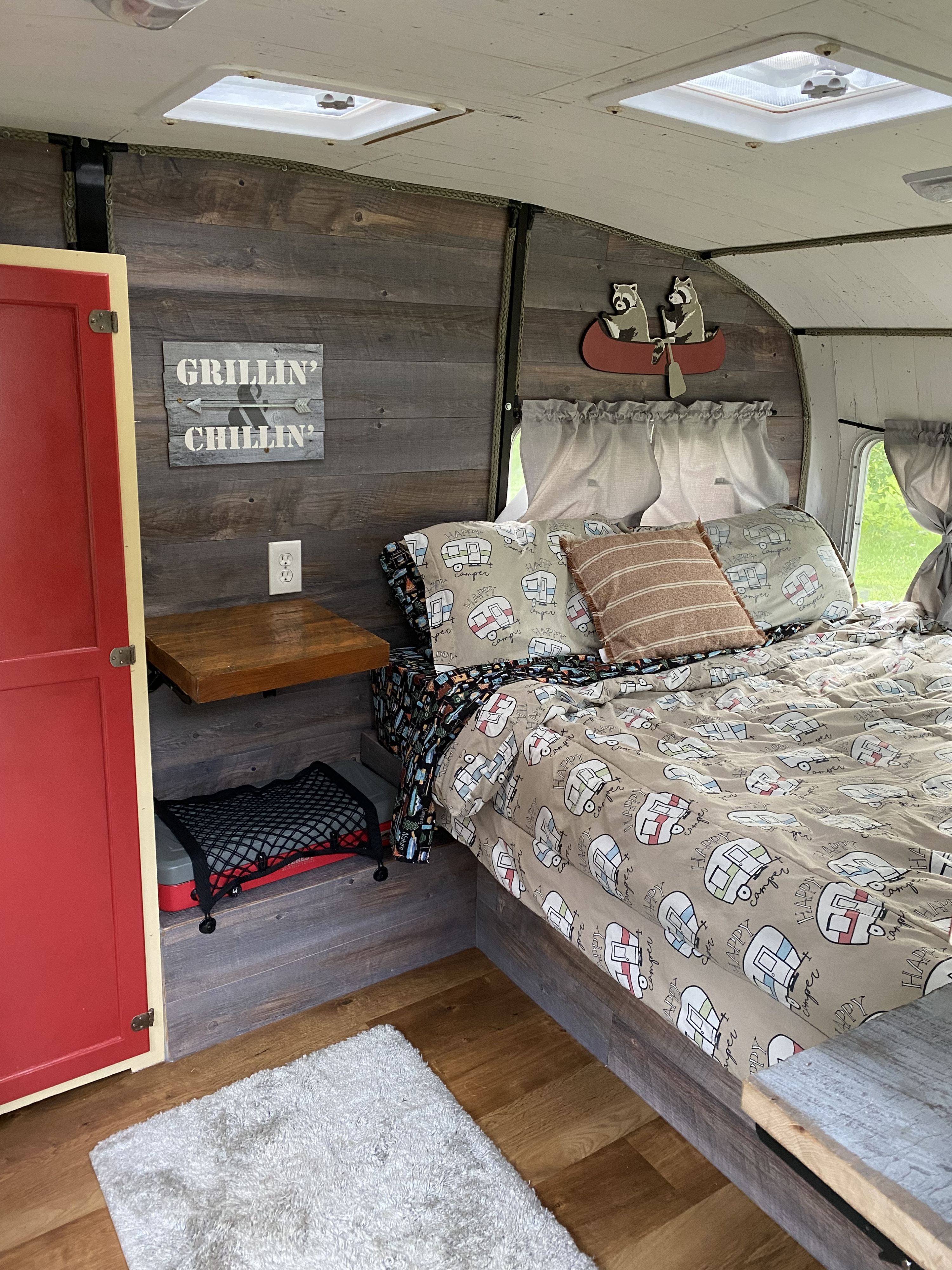 Inviting RV rental interior: a comfy bed with camper print, rustic wood walls, and cute "Grillin' & Chillin'" decor.. Shasta Cygnet 1973