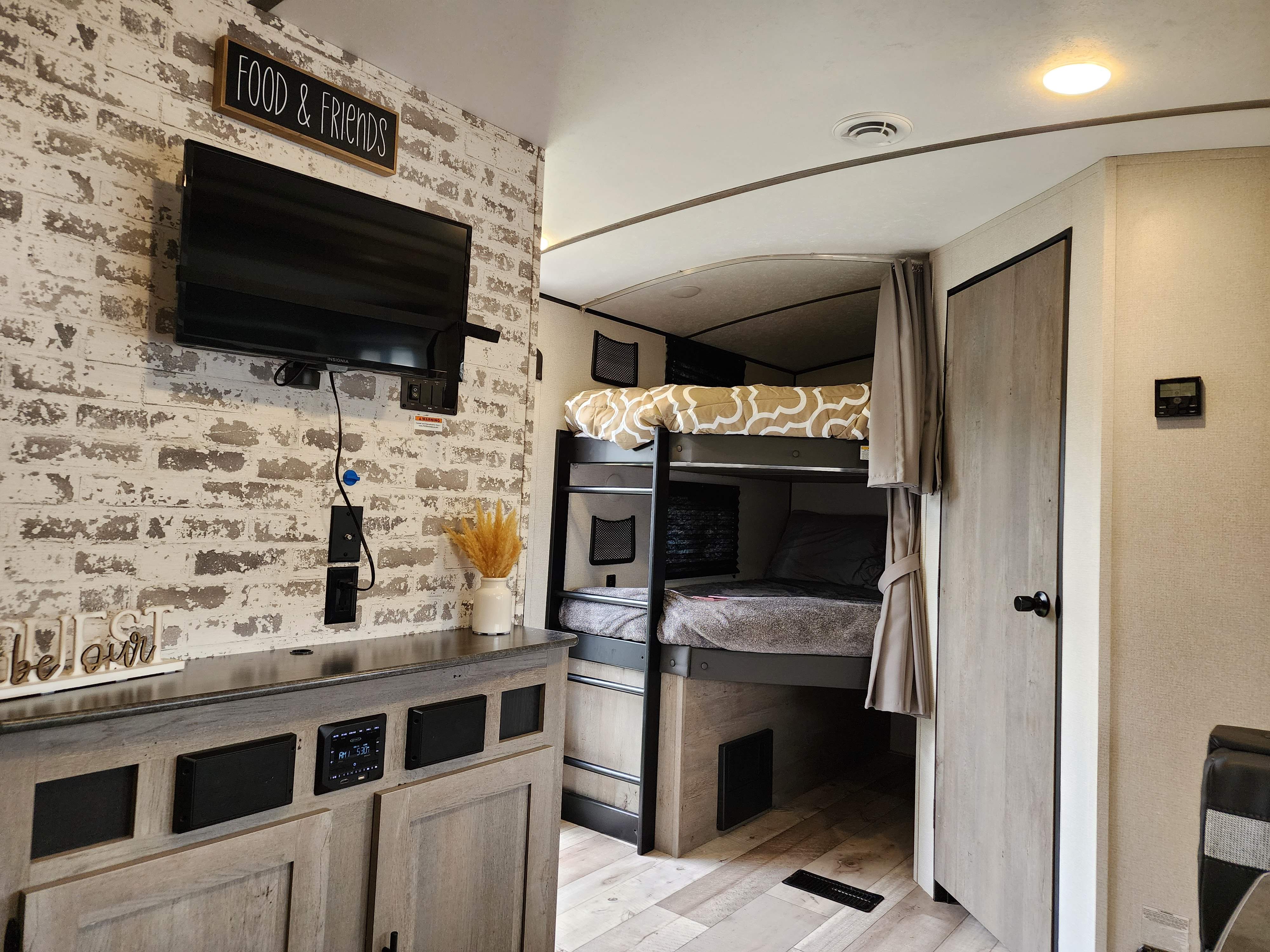 Cozy RV rental interior: bunk beds with privacy curtains, entertainment center with TV, and a rustic brick accent wall.. Keystone RV Springdale 2021
