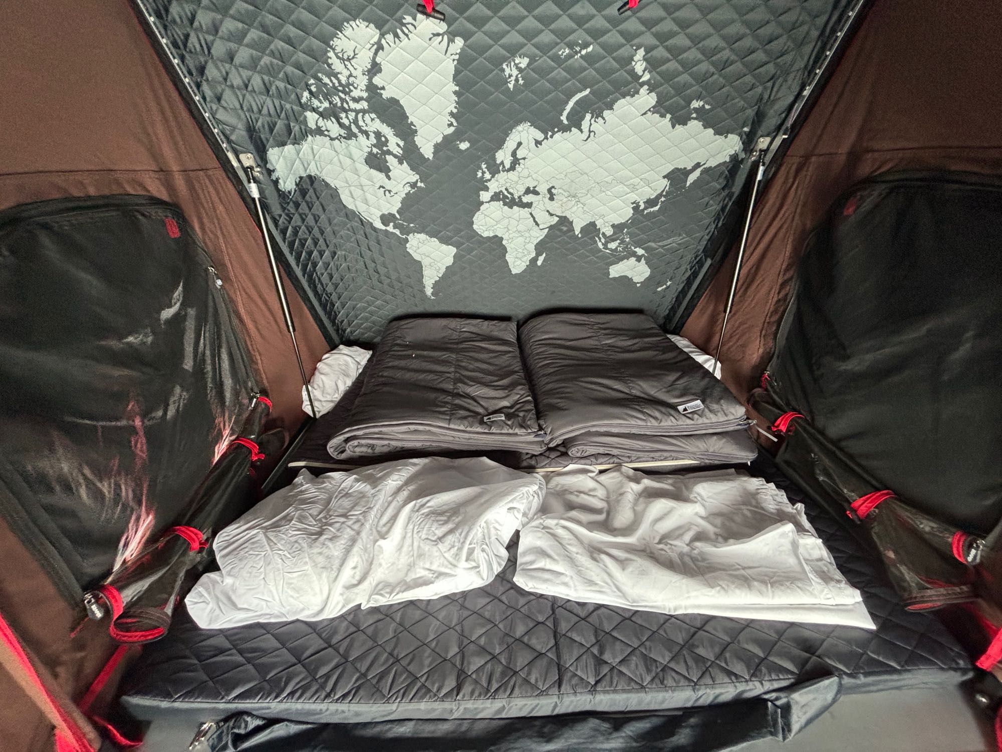 Cozy interior of an RV rental tent, featuring a world map ceiling, sleeping bags, and a comfortable mattress for travel adventures.. Subaru Outback Wilderness 2023