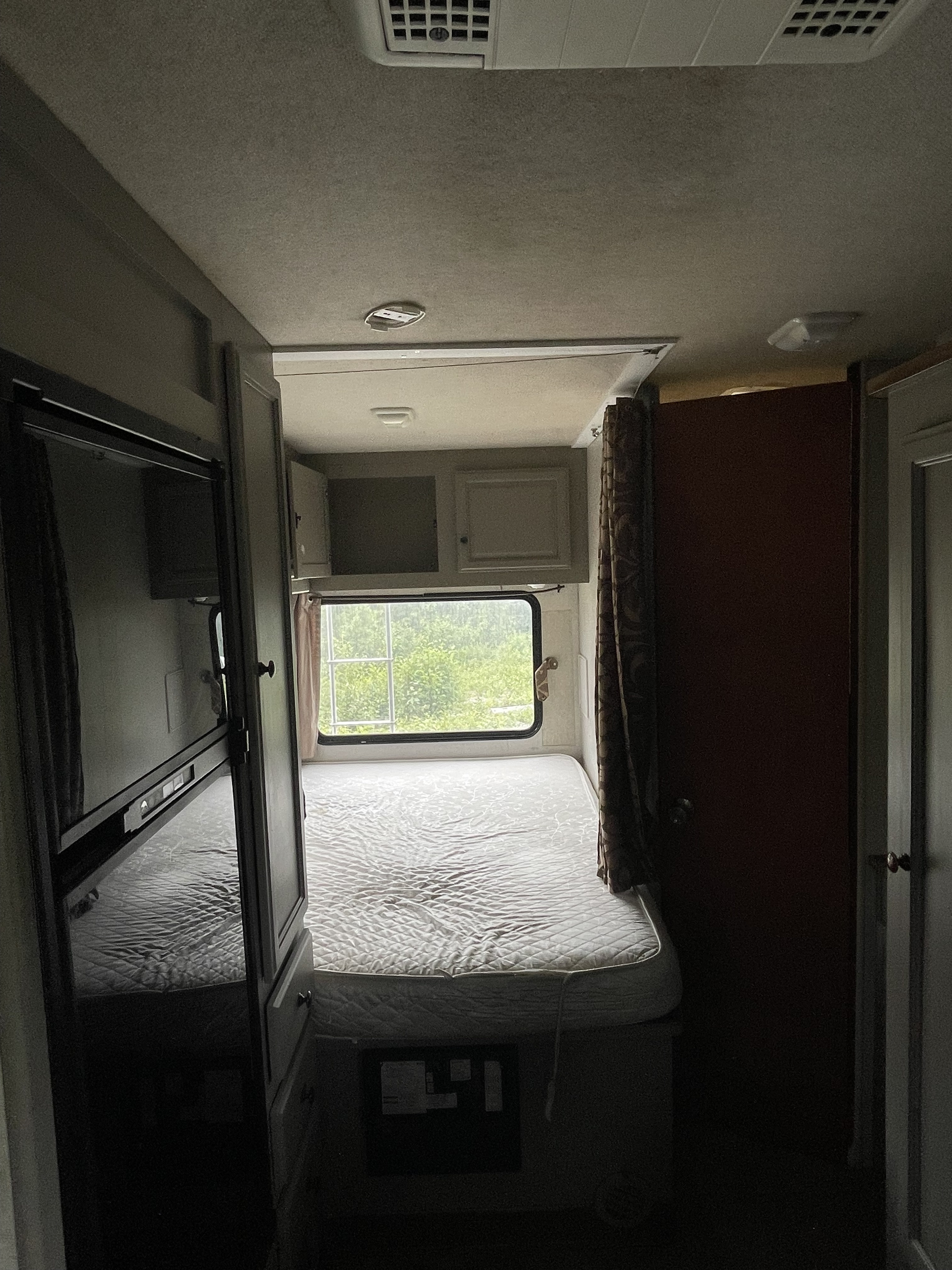 Interior of an RV rental: a bright bedroom with a quilted mattress, window revealing lush trees, and storage cabinets.. Tioga Ranger 2011