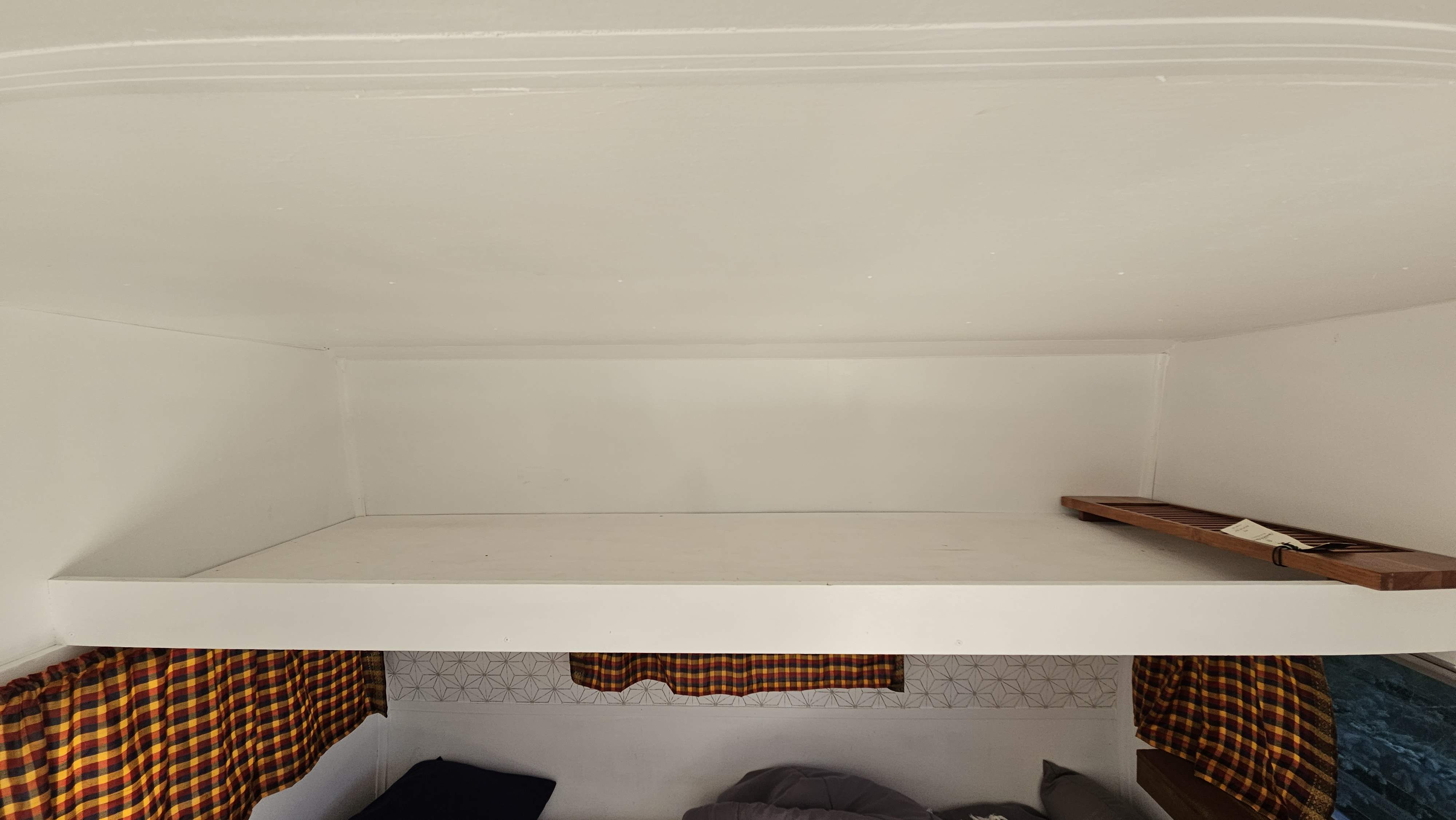 Cozy rv rental bunk bed area with plaid curtains & decorative wall pattern. Upper bunk has a wooden tray.. Shasta Airflyte 1967