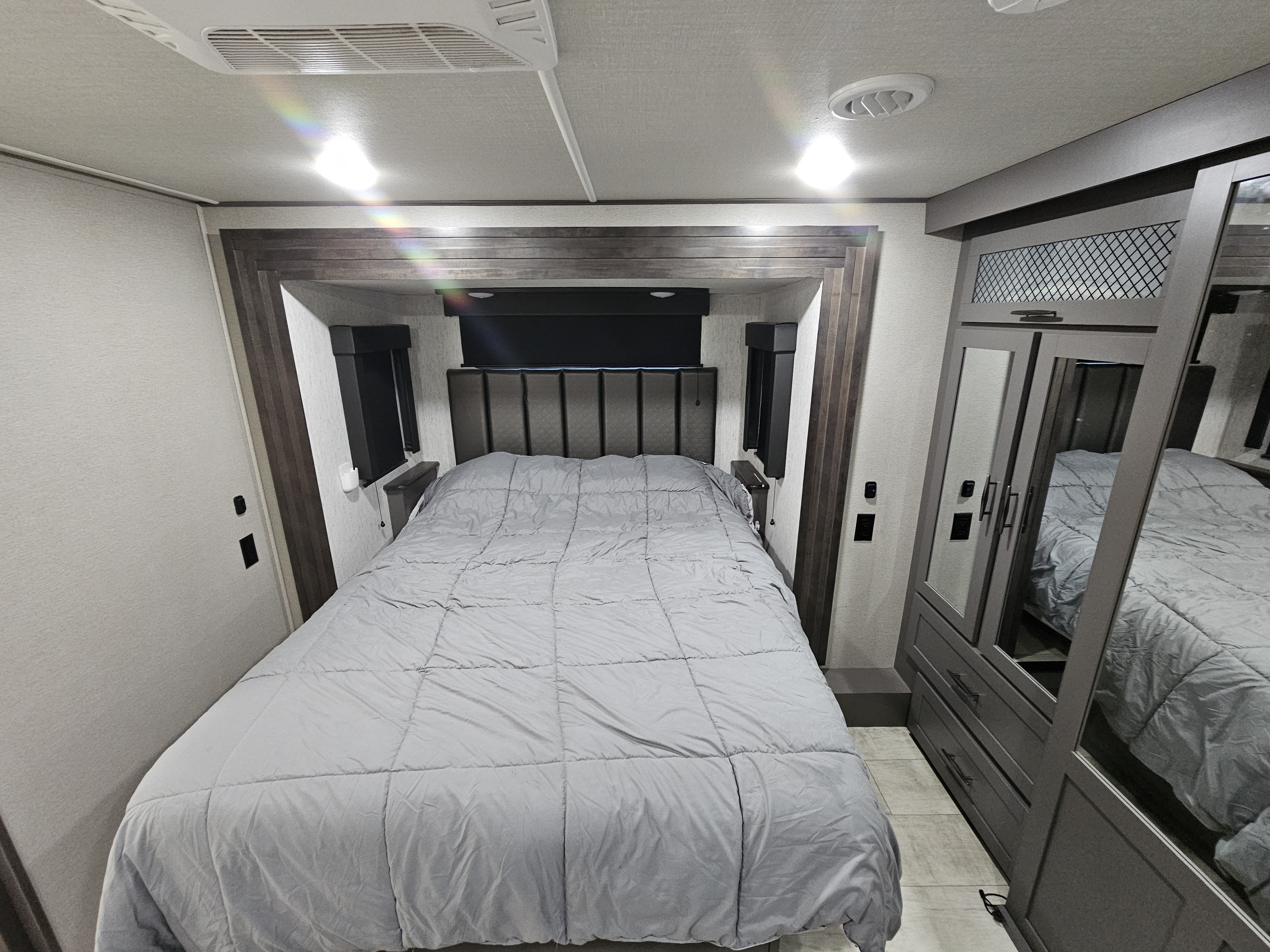 Modern RV rental bedroom featuring a large bed with gray comforter, built-in storage, and mirrored closet. Cozy and functional.. Grand Design Momentum 2022