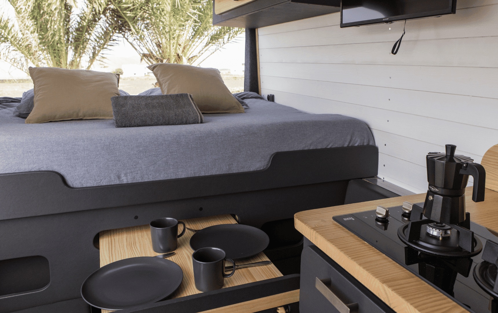 This cozy RV rental interior features a comfy bed, compact kitchen with a stovetop, and a pull-out dining area.. Ford Transit 2023