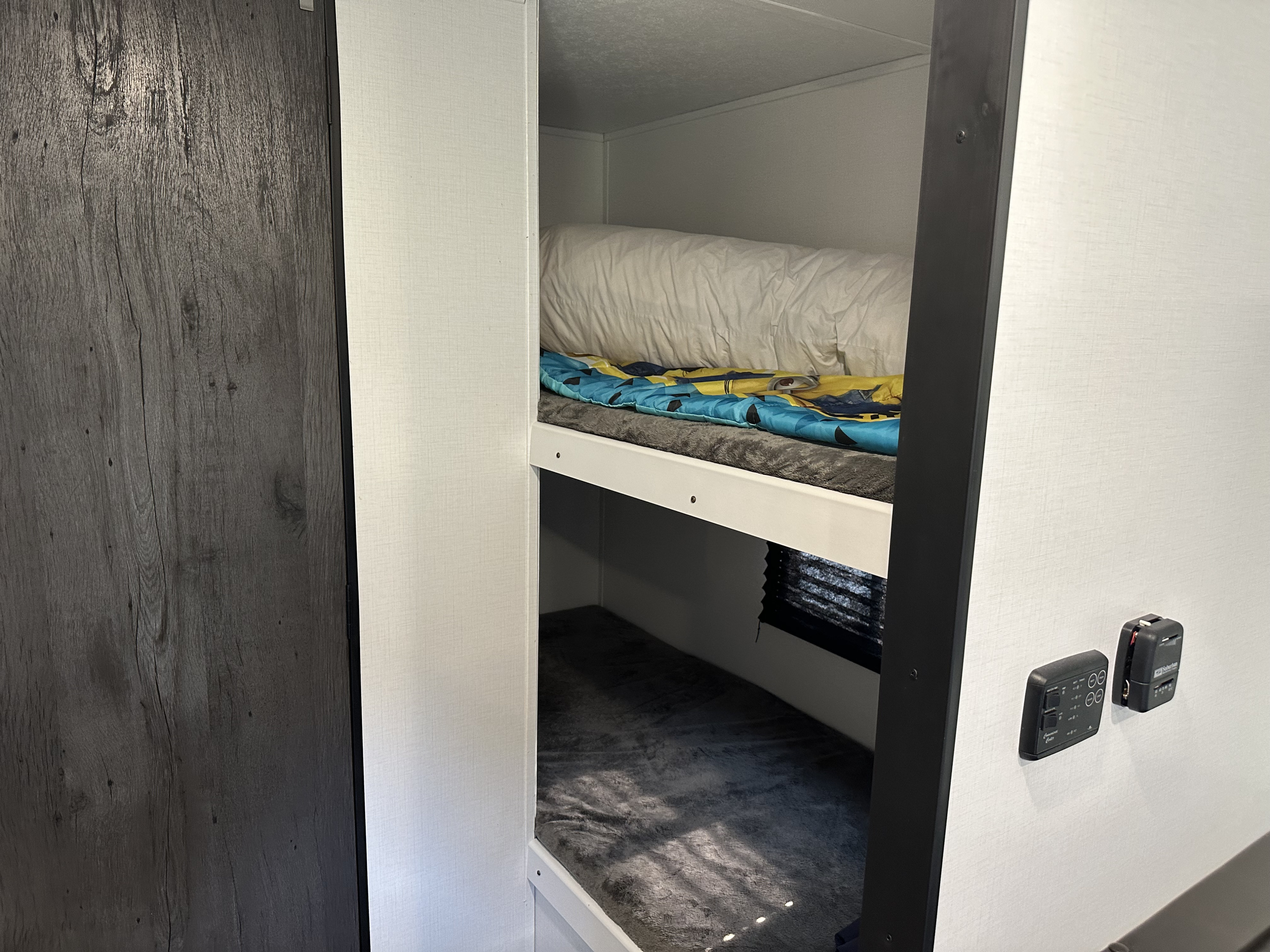 RV rental interior features cozy bunk beds with bedding, plus wall-mounted controls, for a compact living space.. Jayco Jay Flight SLX 2021