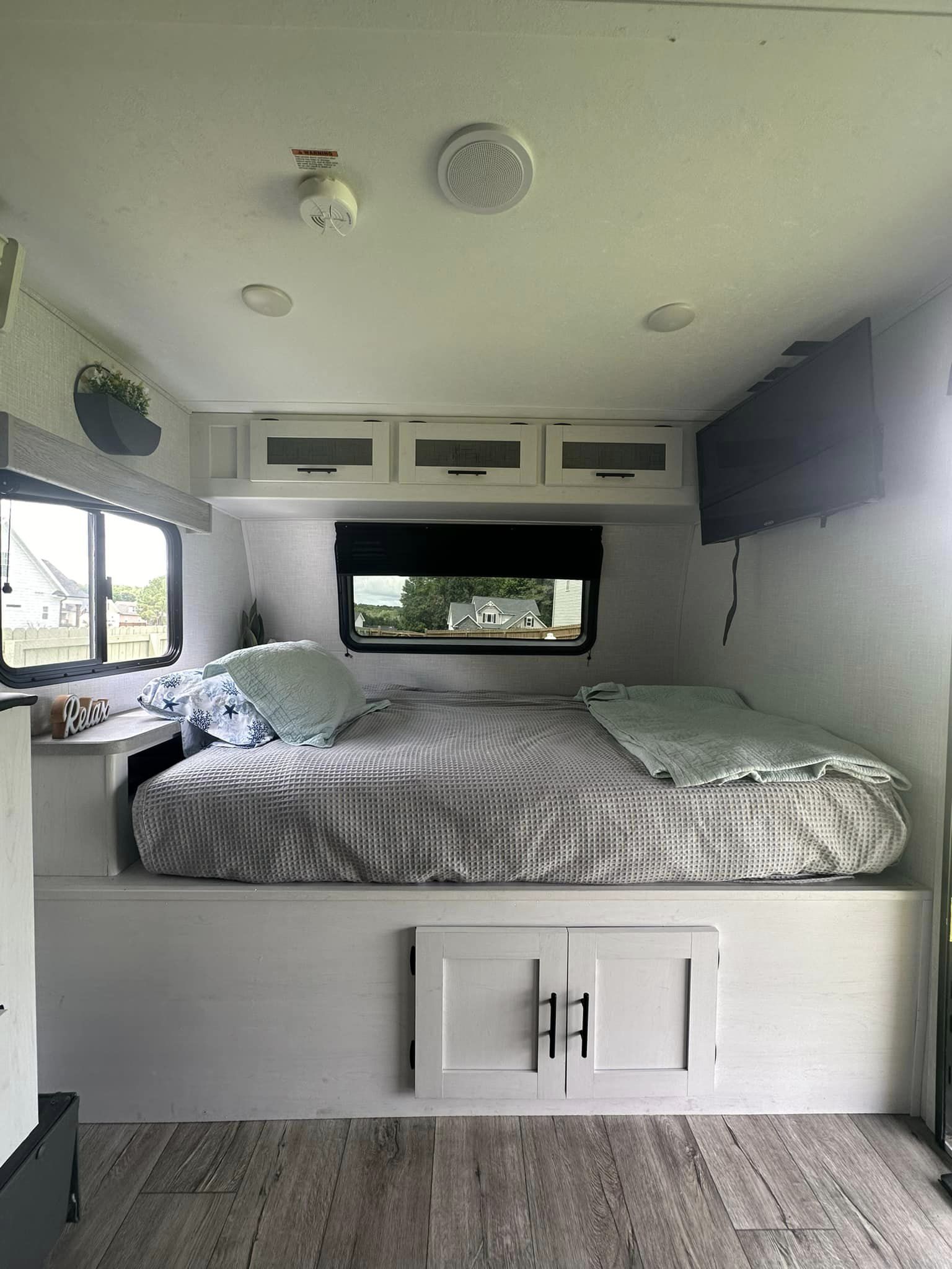 Cozy RV rental bedroom featuring a large bed, windows, overhead cabinets, and a mounted TV.. Coleman by Dutchman Rubicon 1708BH 2024