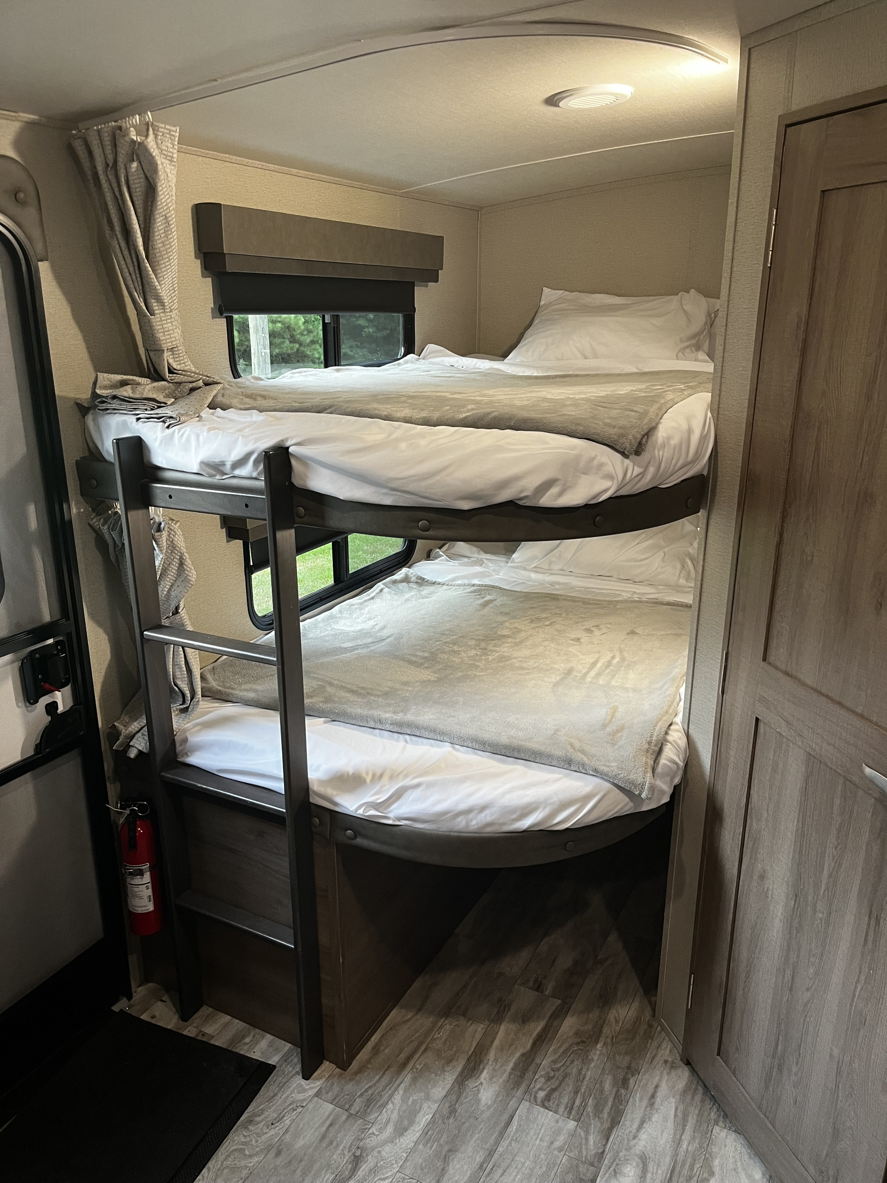 RV rental interior features two bunk beds, neatly made with white sheets and gray blankets. Comfortable sleeping setup.. Grand Design Imagine 2021