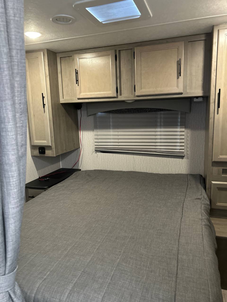 Experience comfort in this RV rental bedroom, featuring a gray bed, light wood cabinets, and a window with blinds.. Coachman Freelander 2022