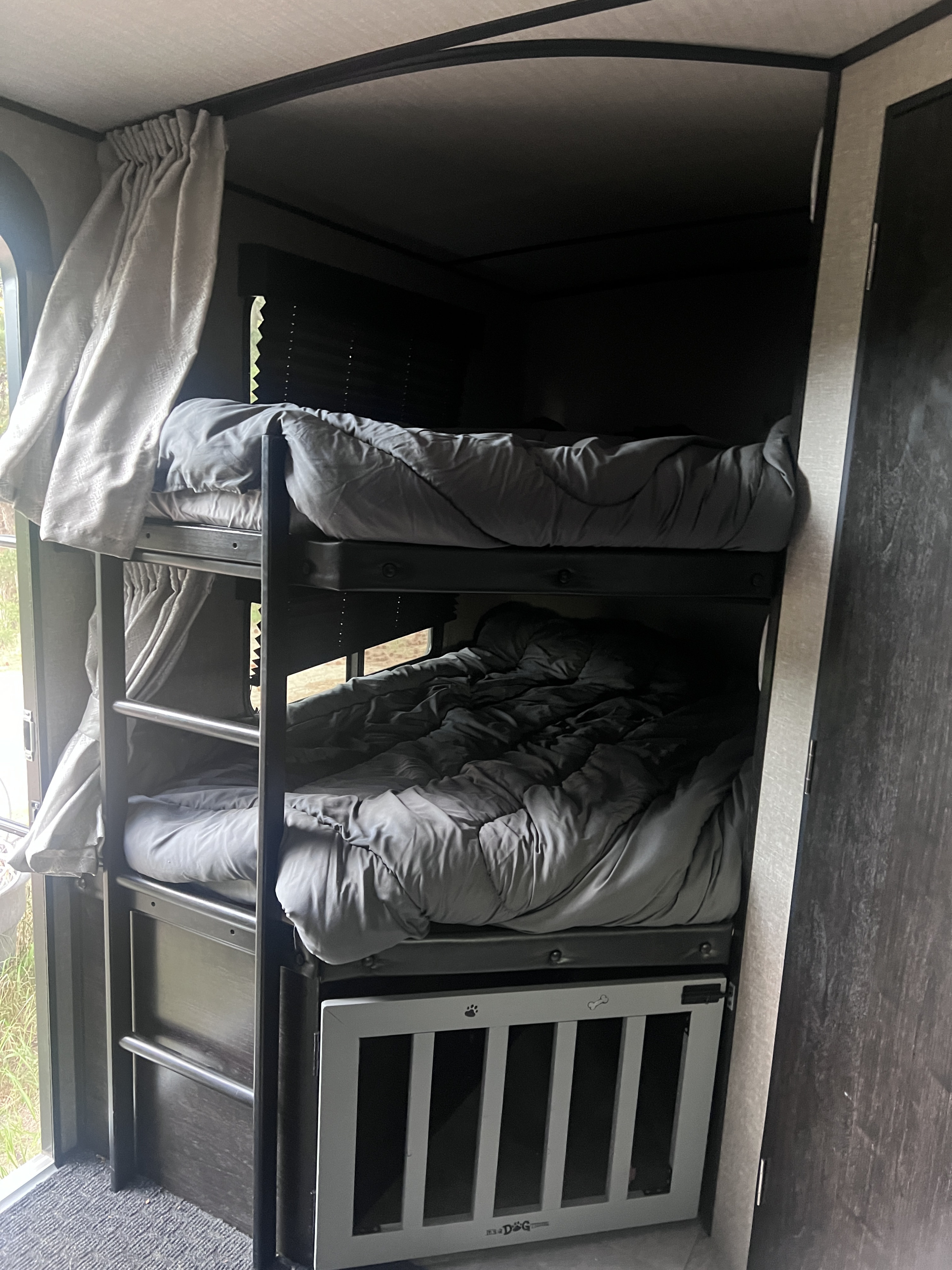 Cozy RV rental bunk beds with grey bedding, plus a handy dog crate built-in below. Great for family trips.. Grand Design Imagine 2020