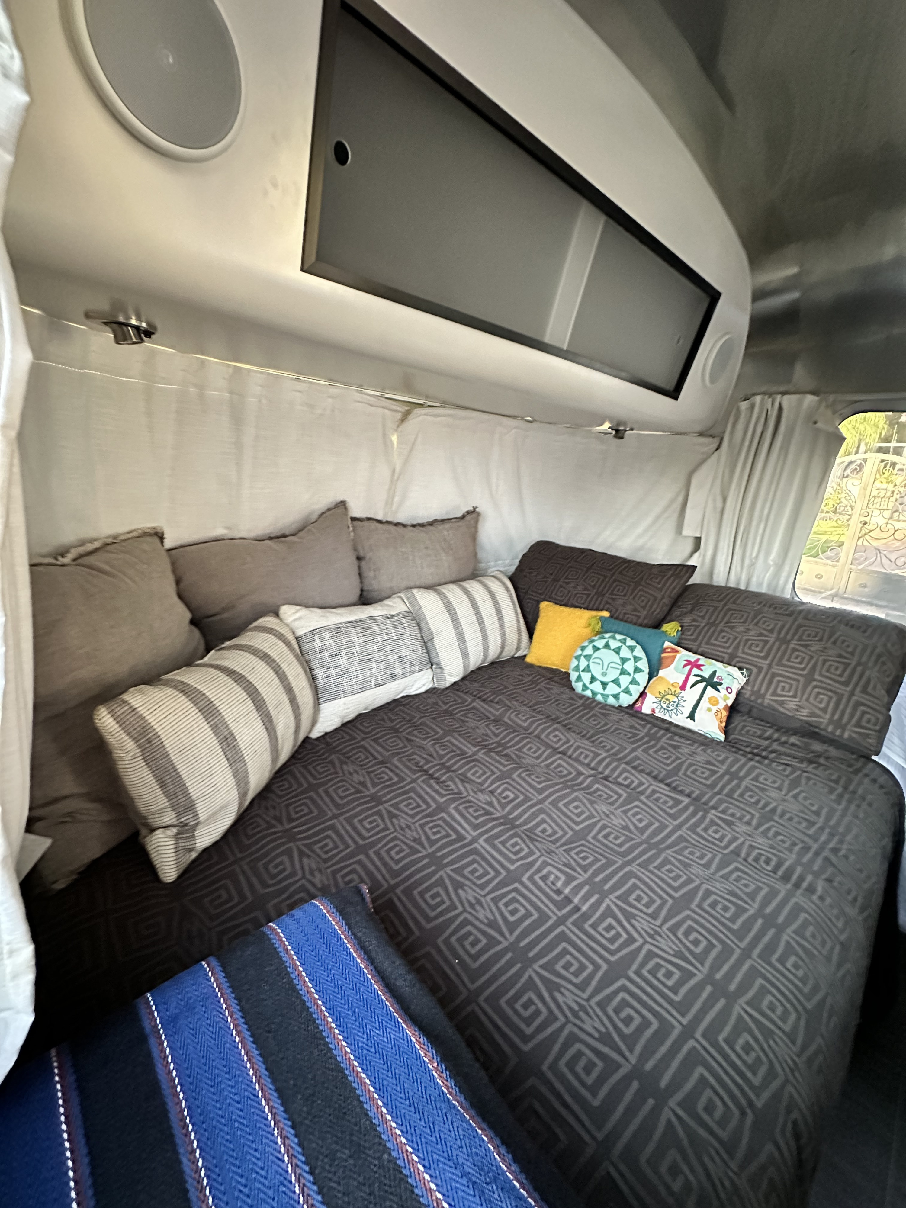 Modern Airstream RV rental interior: a comfy bed with geometric duvet, colorful pillows, and smart overhead features.. Airstream Caraval 2021