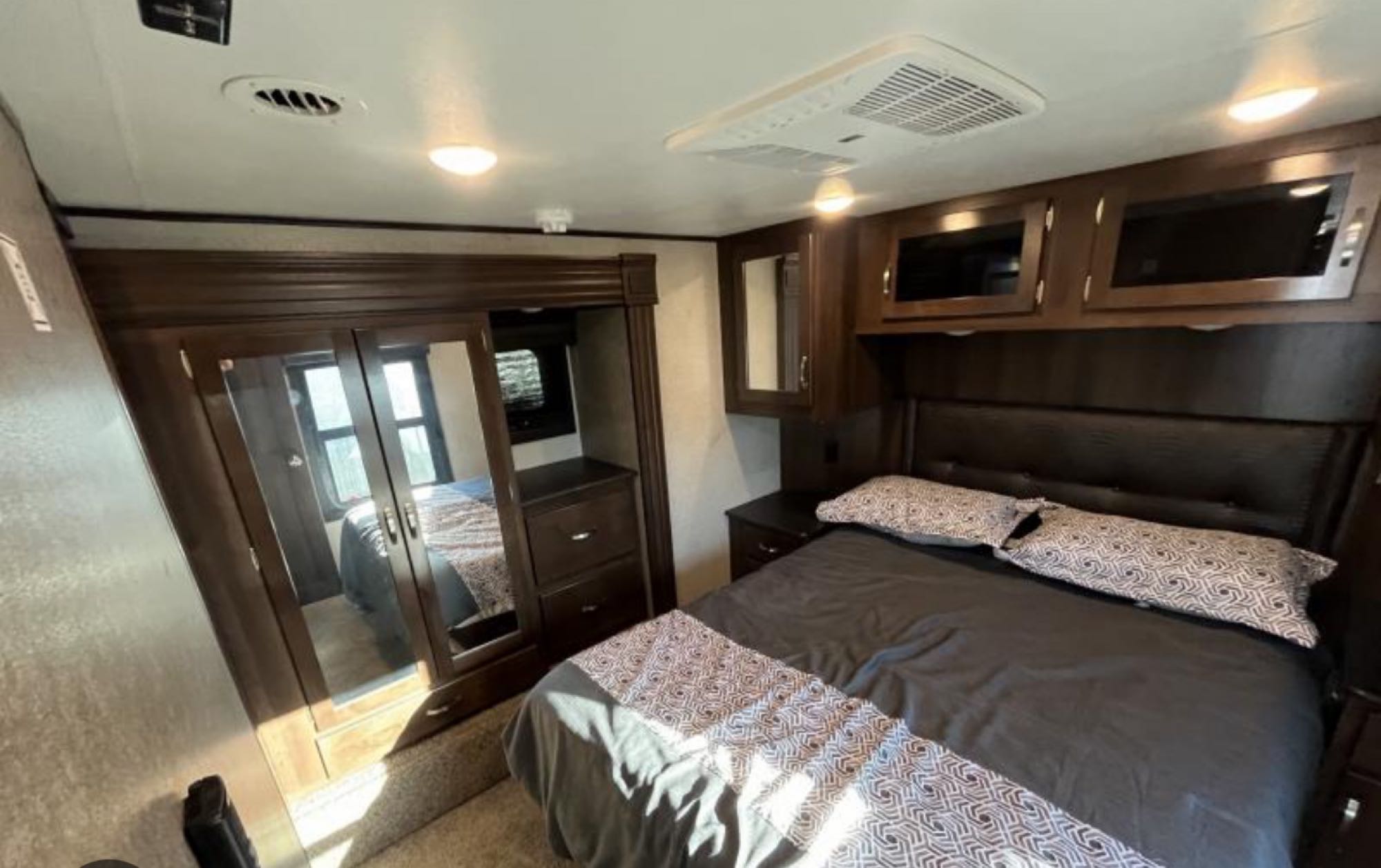 Experience comfort in this modern RV rental bedroom. Features a cozy bed, dark wood storage, mirrored closet, and bright lighting.. Jayco Talon 2019