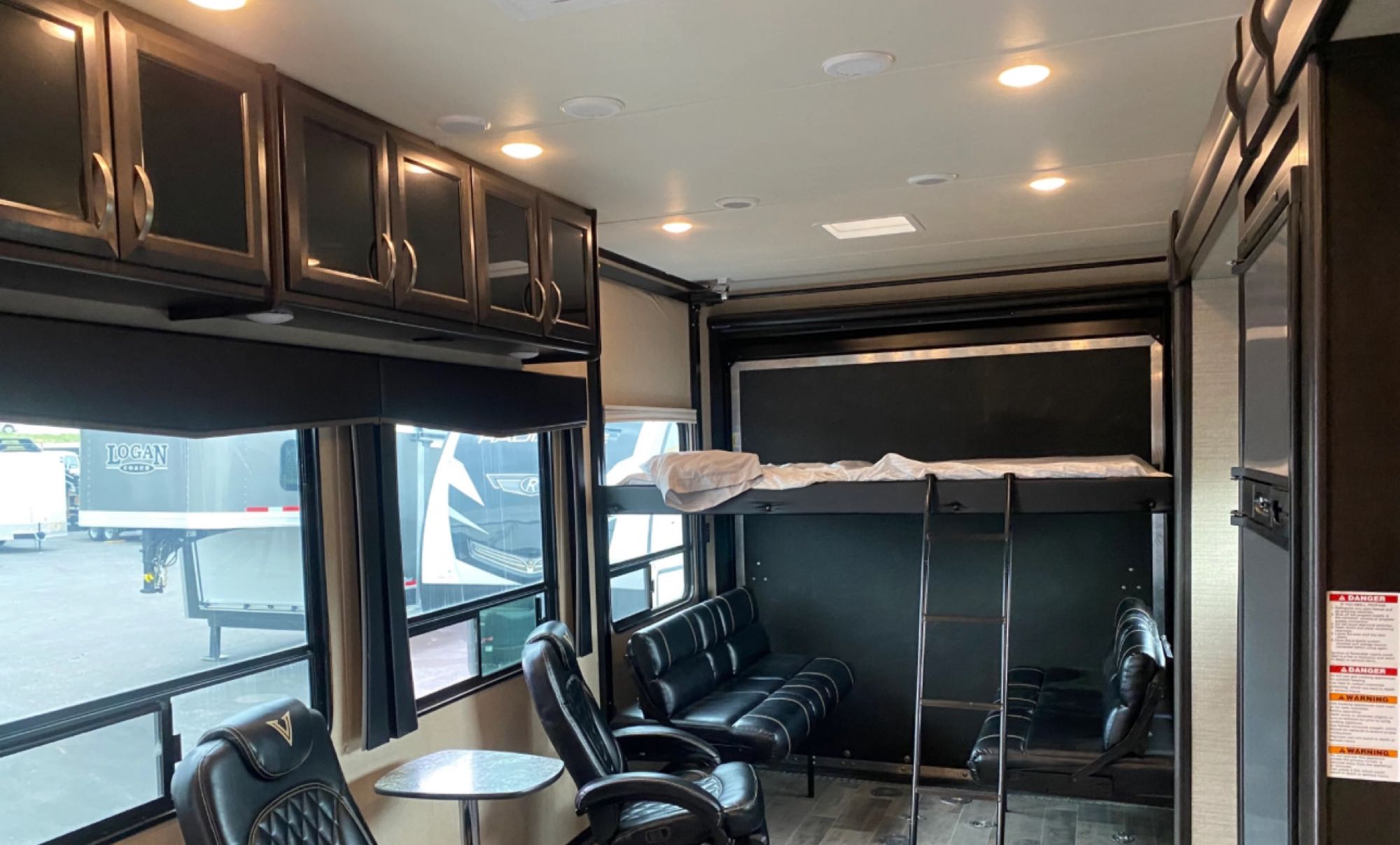 Inside an RV rental: dark wood cabinets, large windows, a comfy armchair, sofa, and bunk bed with ladder.. Jayco Talon 2019