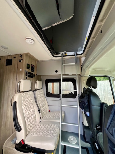 RV rental interior: A ladder leads to the overhead bed, flanked by quilted passenger seats & a control panel on the wall.. Winnebago Winnebago 2023
