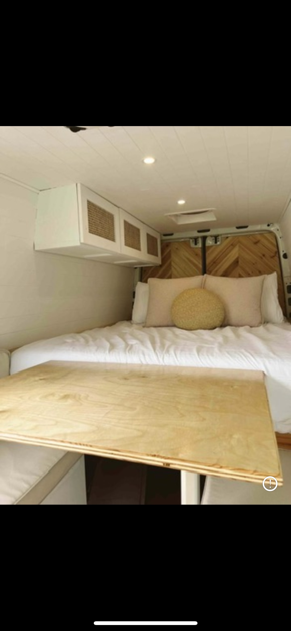 Cozy RV rental interior: bed with pillows, wood herringbone headboard, white overhead cabinets, and a light wood table.. Mercedes Sprinter 2013