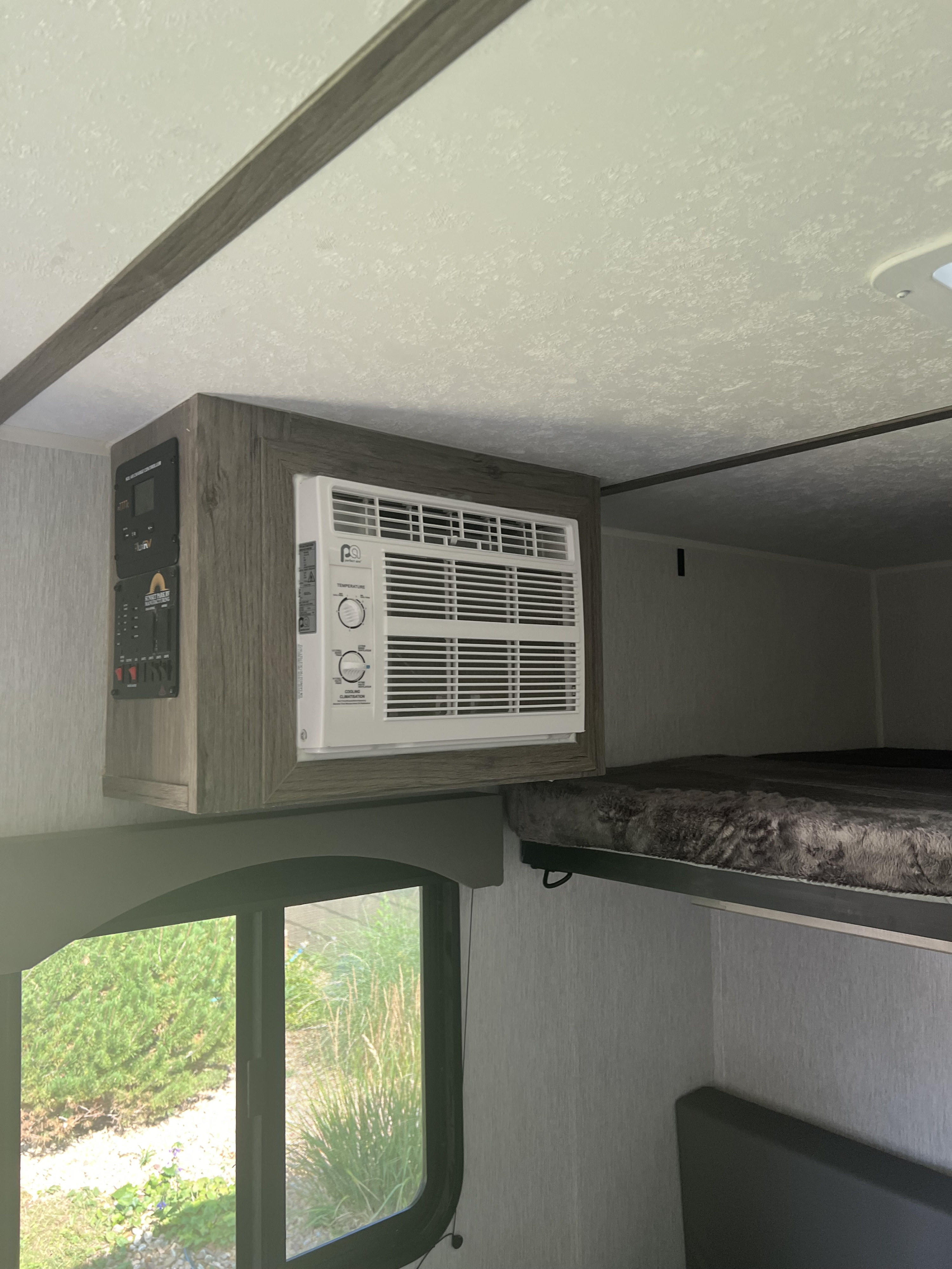 RV rental interior: window AC unit, control panel, window view, and a cozy bunk bed setup.. Sunset RV park Sunray 129 2025