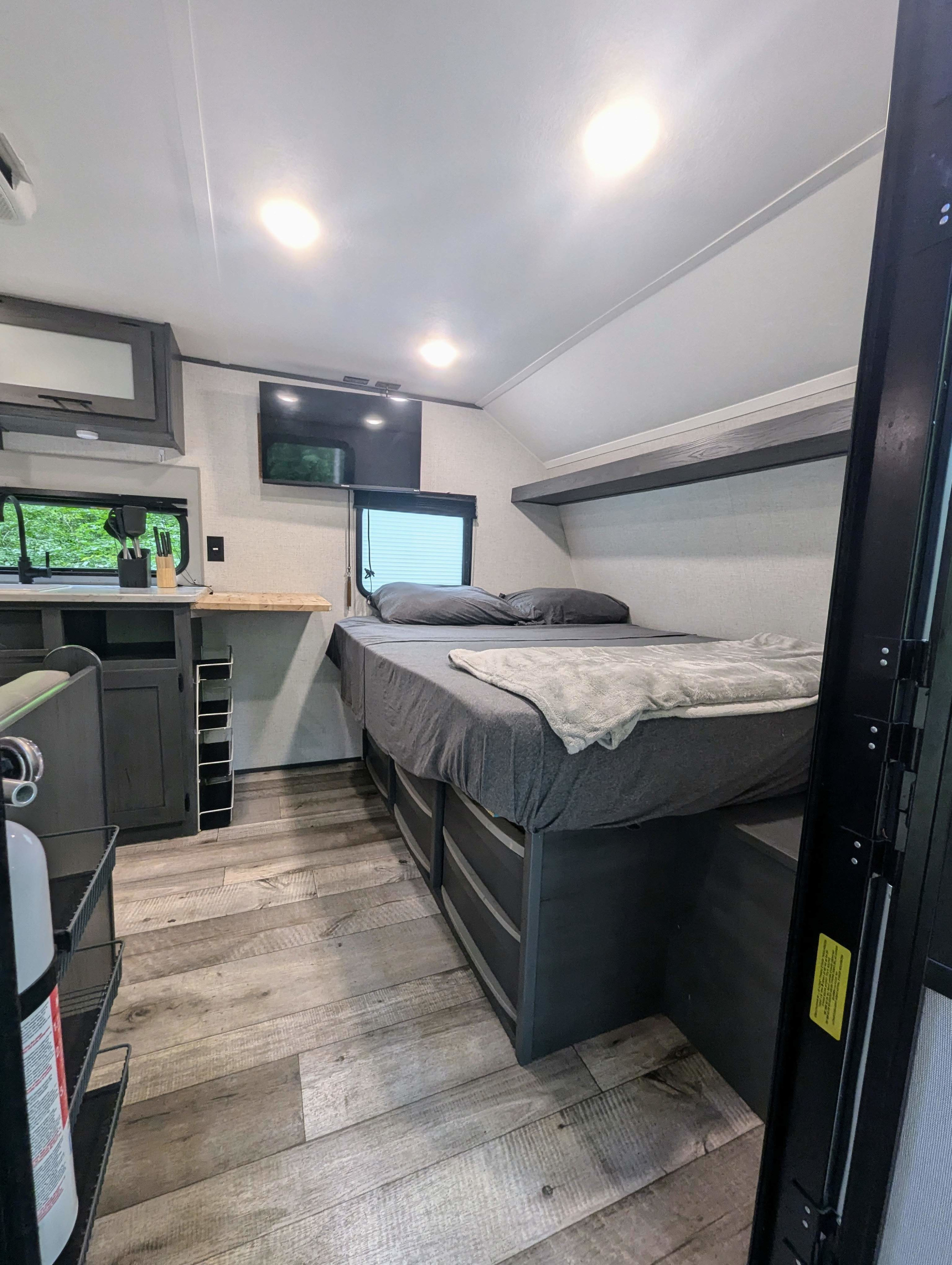 RV rental cozy interior: full bed with storage drawers, shelf, wall-mounted TV, & kitchen. Wood-look floor.. Aspen Trail LE 2022