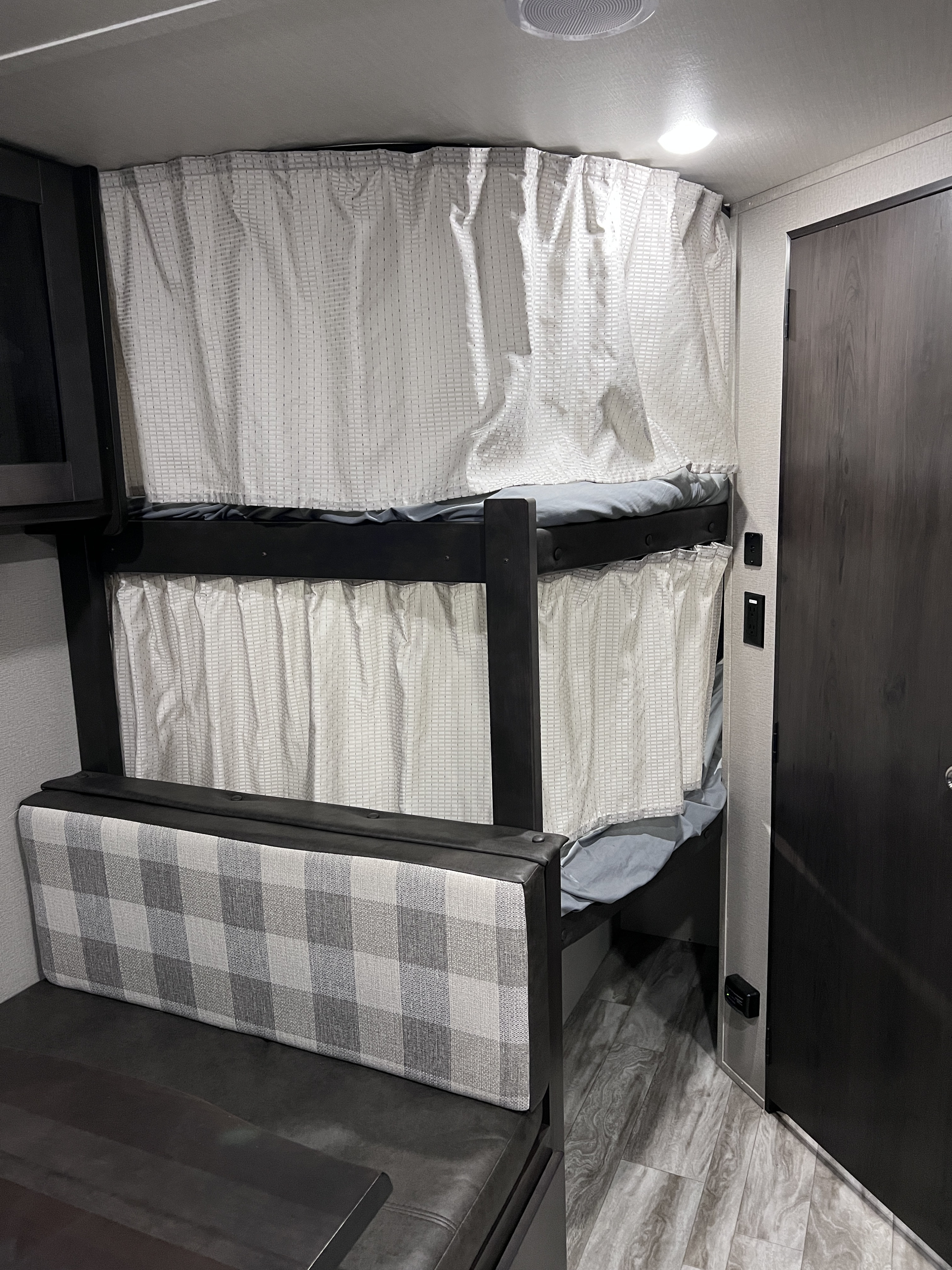 Cozy RV rental interior with bunk beds featuring light grey patterned privacy curtains, a checkered dinette, and wood-look flooring.. Grand Design Transcend Xplor 2021