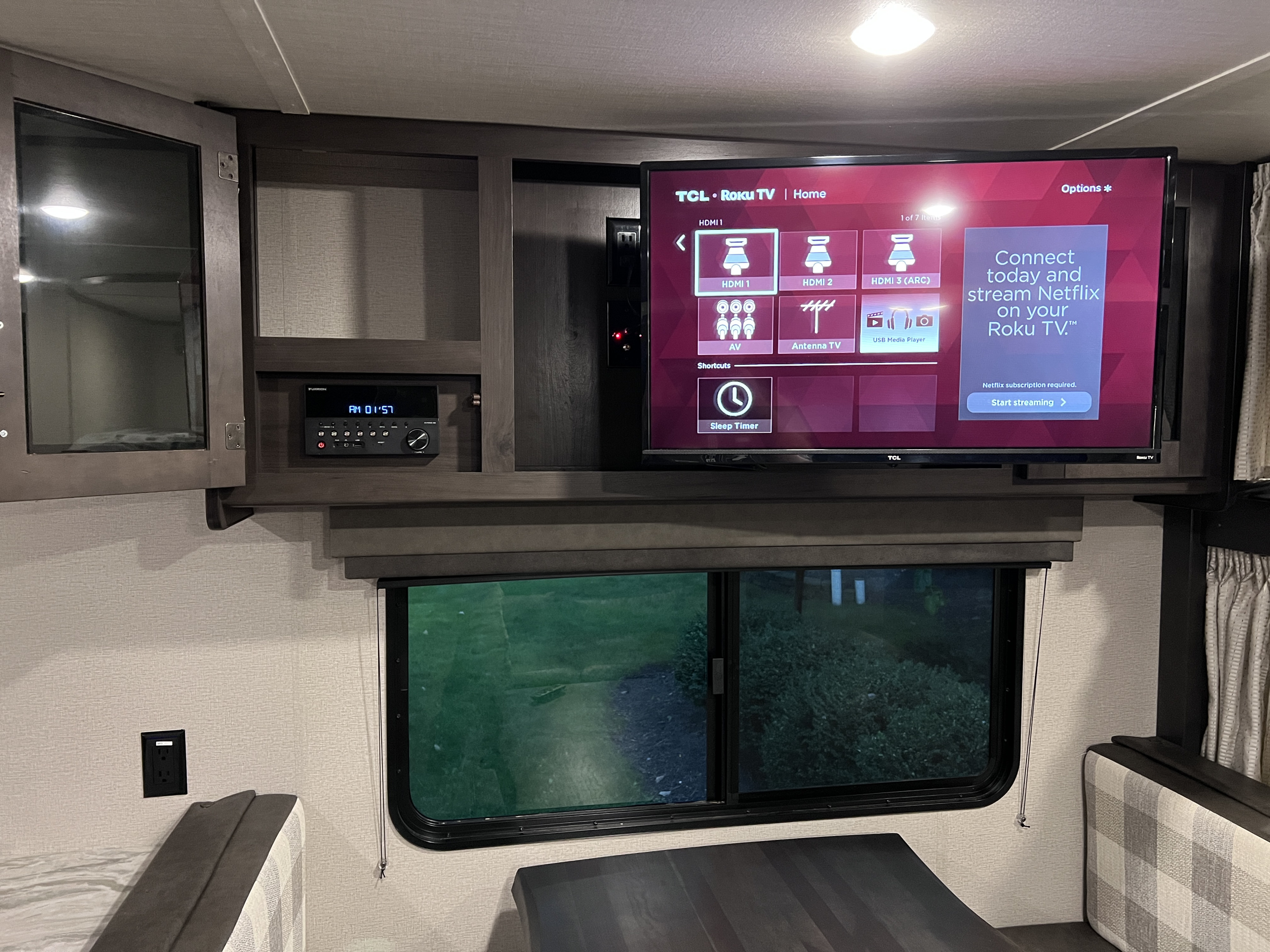 **RV rental** interior: A TCL Roku TV and Furrion stereo system offer entertainment, positioned above a window with a green view.. Grand Design Transcend Xplor 2021