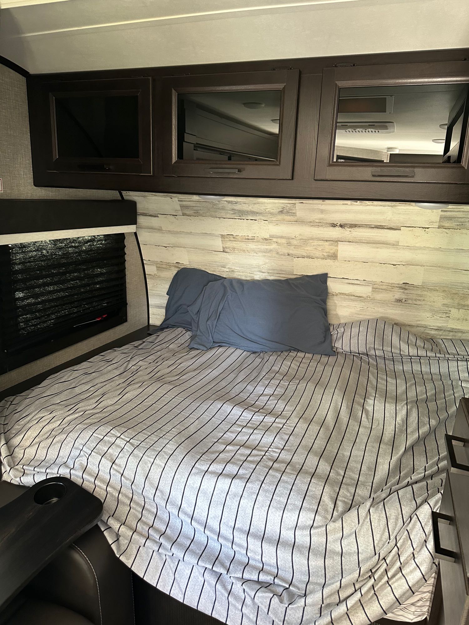 RV rental bedroom: a cozy space with a striped bed, blue pillow, and dark overhead storage cabinets.. Jayco Jay Feather Micro 2022