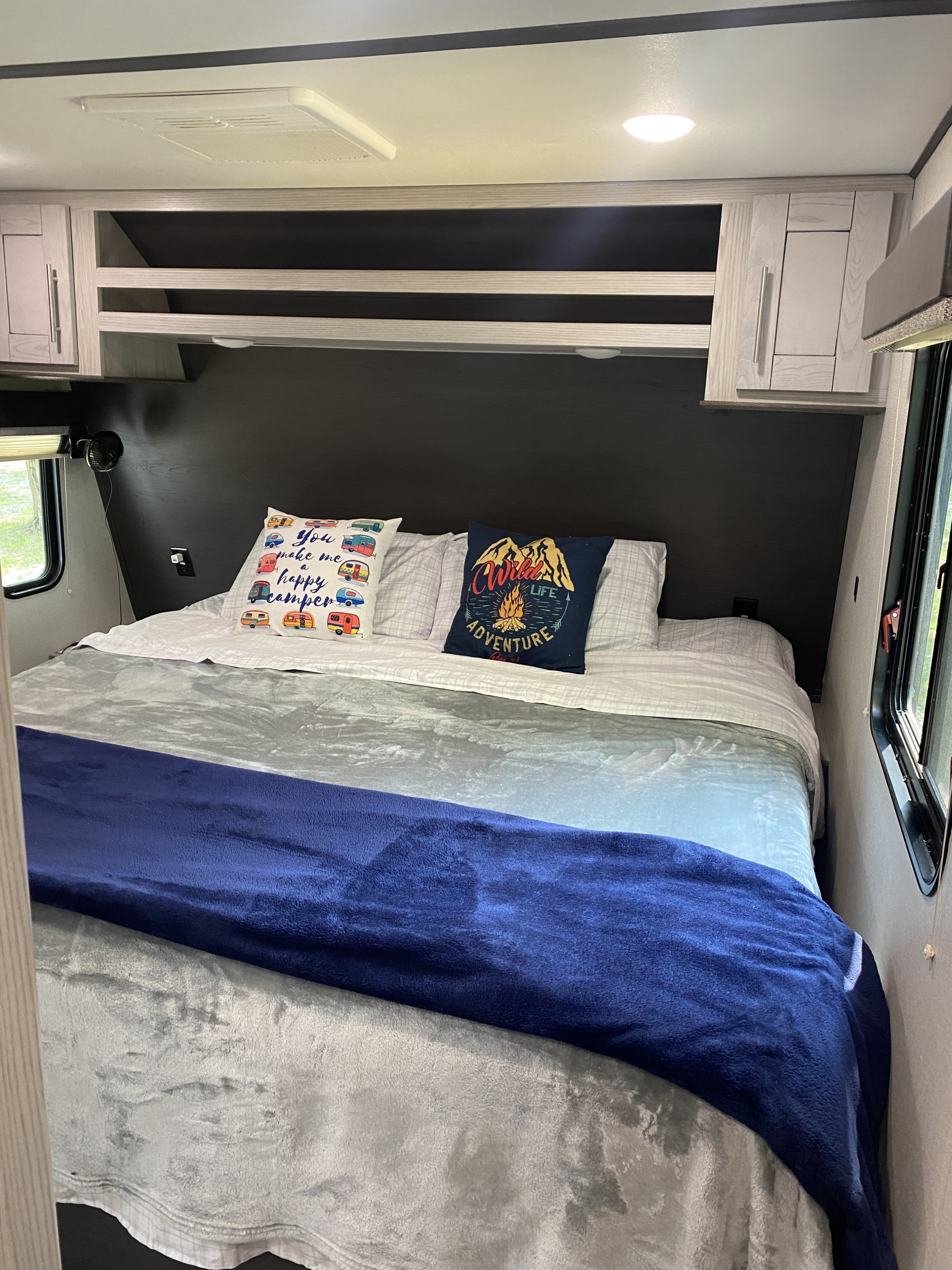Cozy RV rental bedroom featuring a large bed with soft blankets, decorative pillows, overhead storage, and a window for natural light.. Keystone RV Fuzion Impact Toy Hauler 2021