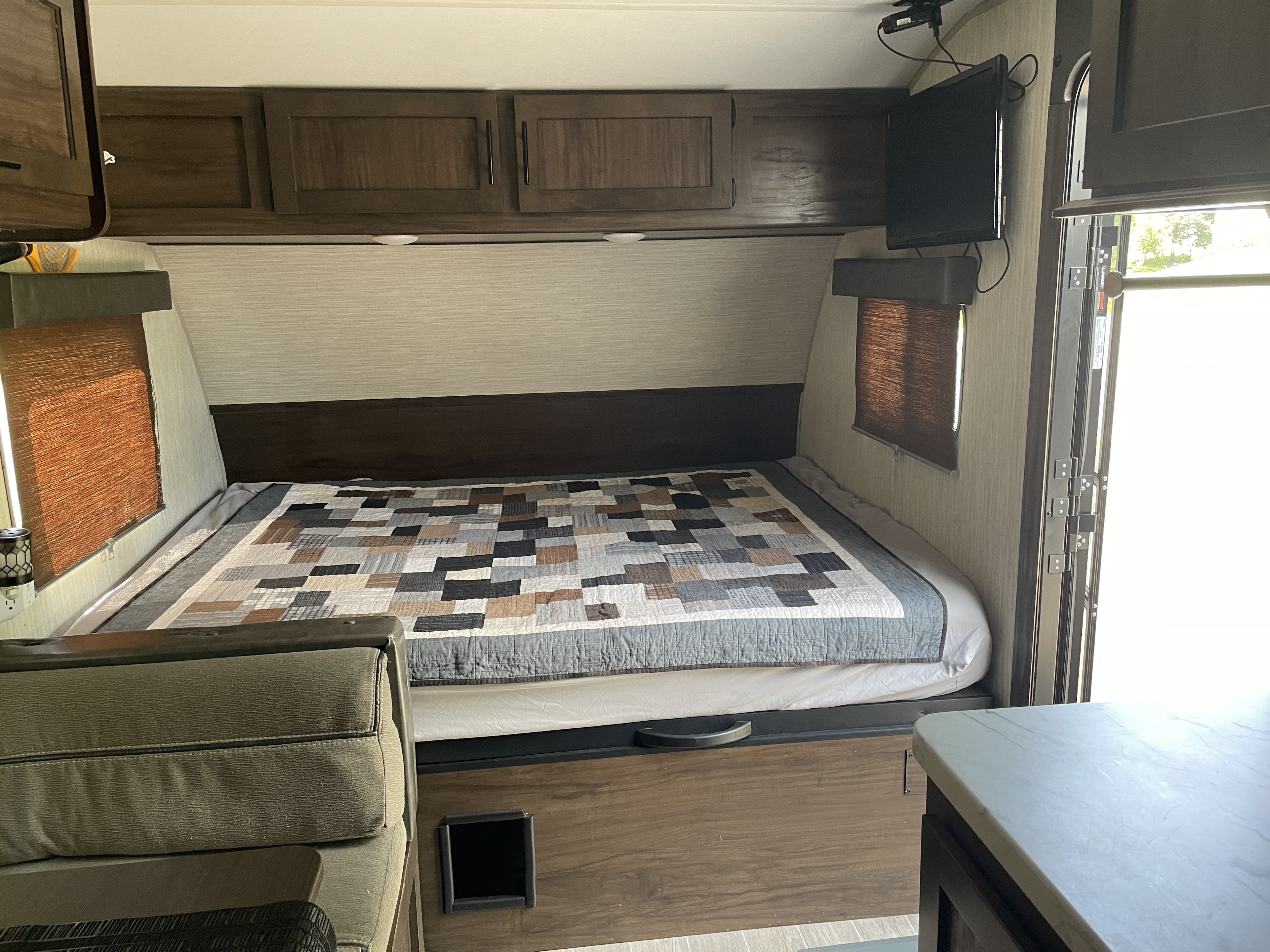 Experience comfort in this RV rental bedroom: quilted bed, overhead cabinets, & TV for relaxing travels.. Forest River Cherokee Wolf Pup BHS 2021