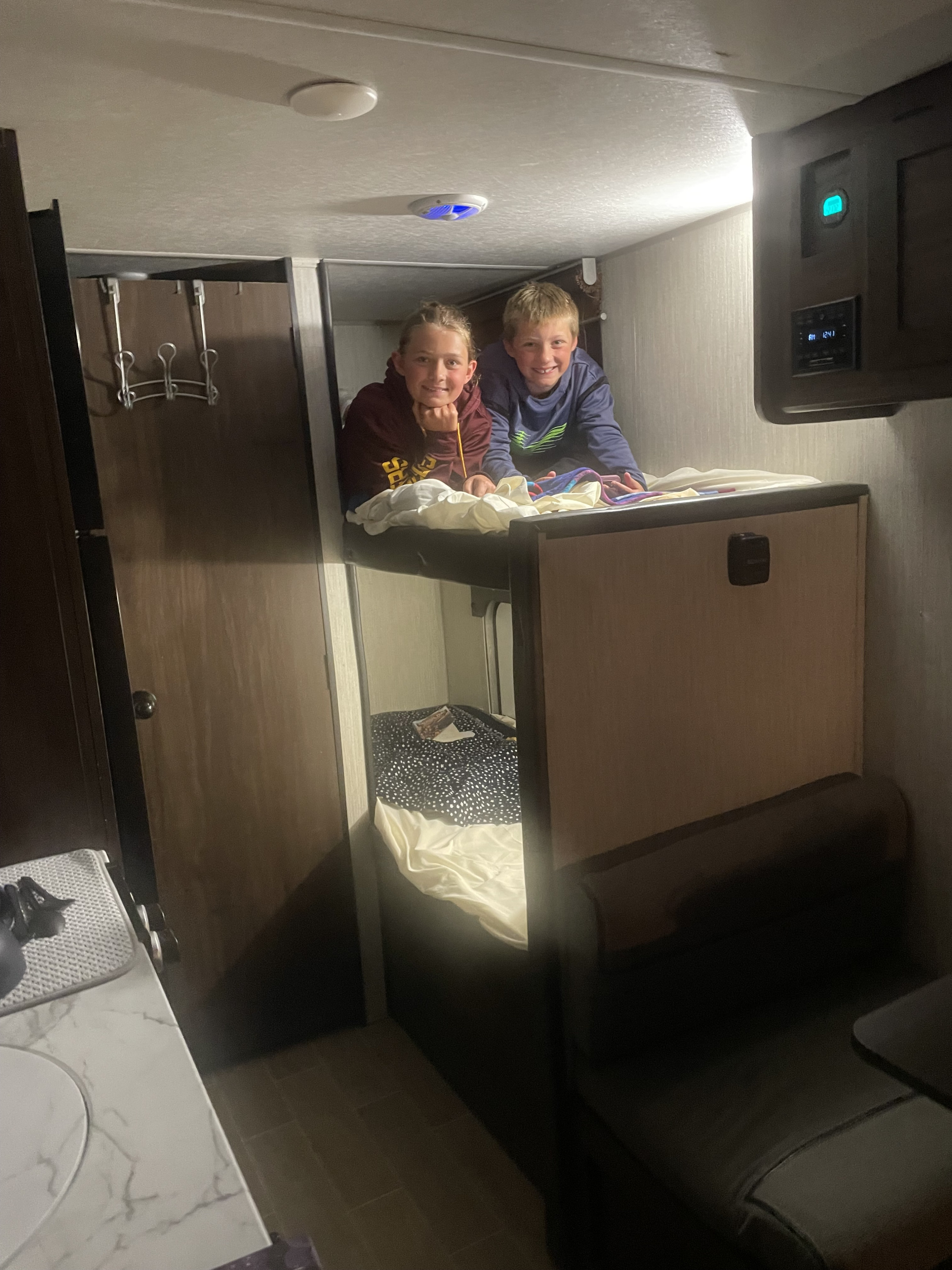 Two kids smiling in bunk beds inside an RV rental, showcasing a cozy camper interior.. Forest River Cherokee Wolf Pup BHS 2021