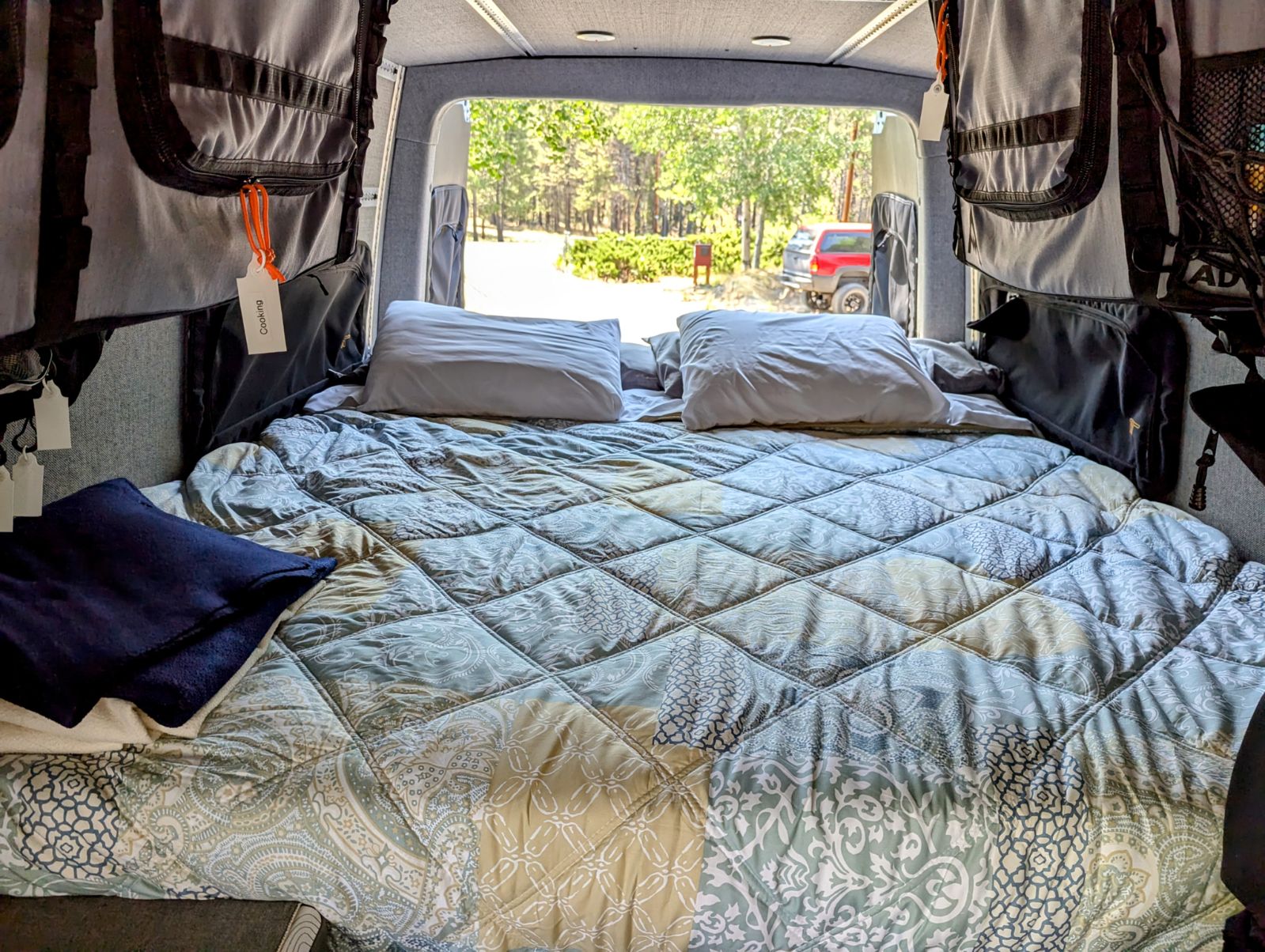 Comfortable RV rental interior with a cozy bed, looking out to a scenic campsite. Perfect for your next adventure.. Winnebago Adventure Wagon 2023