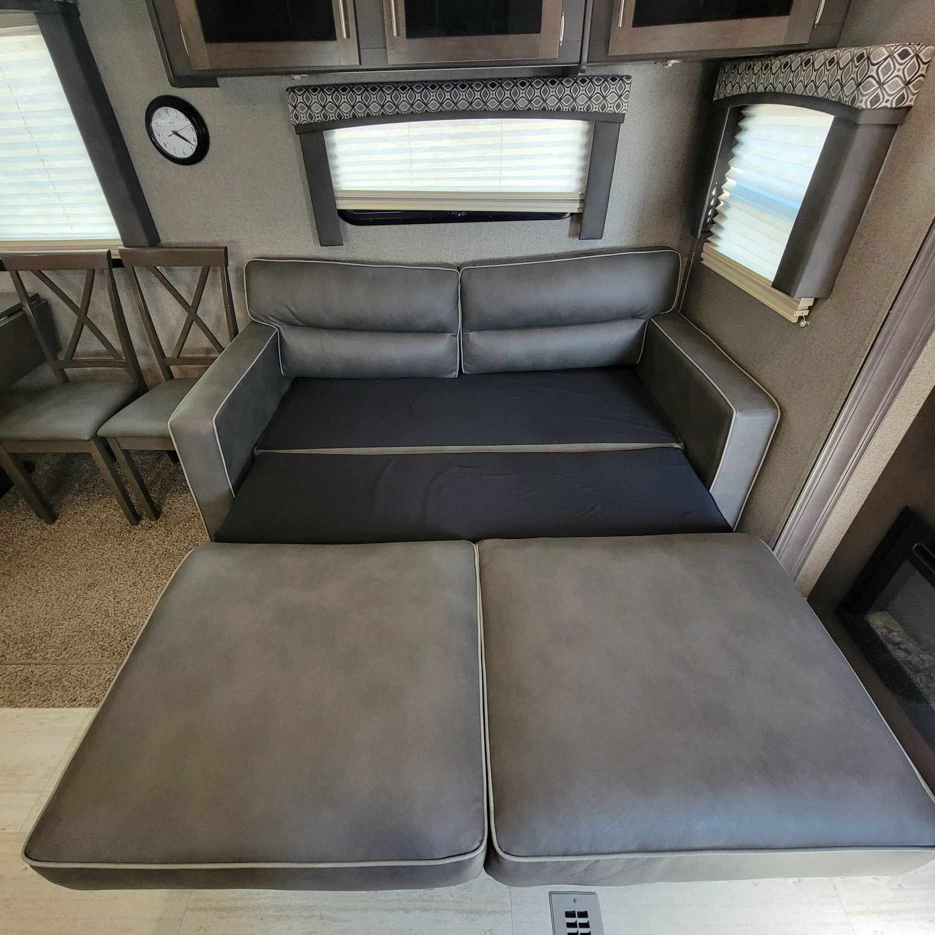 This RV rental features a versatile gray pull-out sofa bed, ideal for extra sleeping space, with chairs and overhead cabinets visible.. Forest River Flagstaff Super Lite 2019