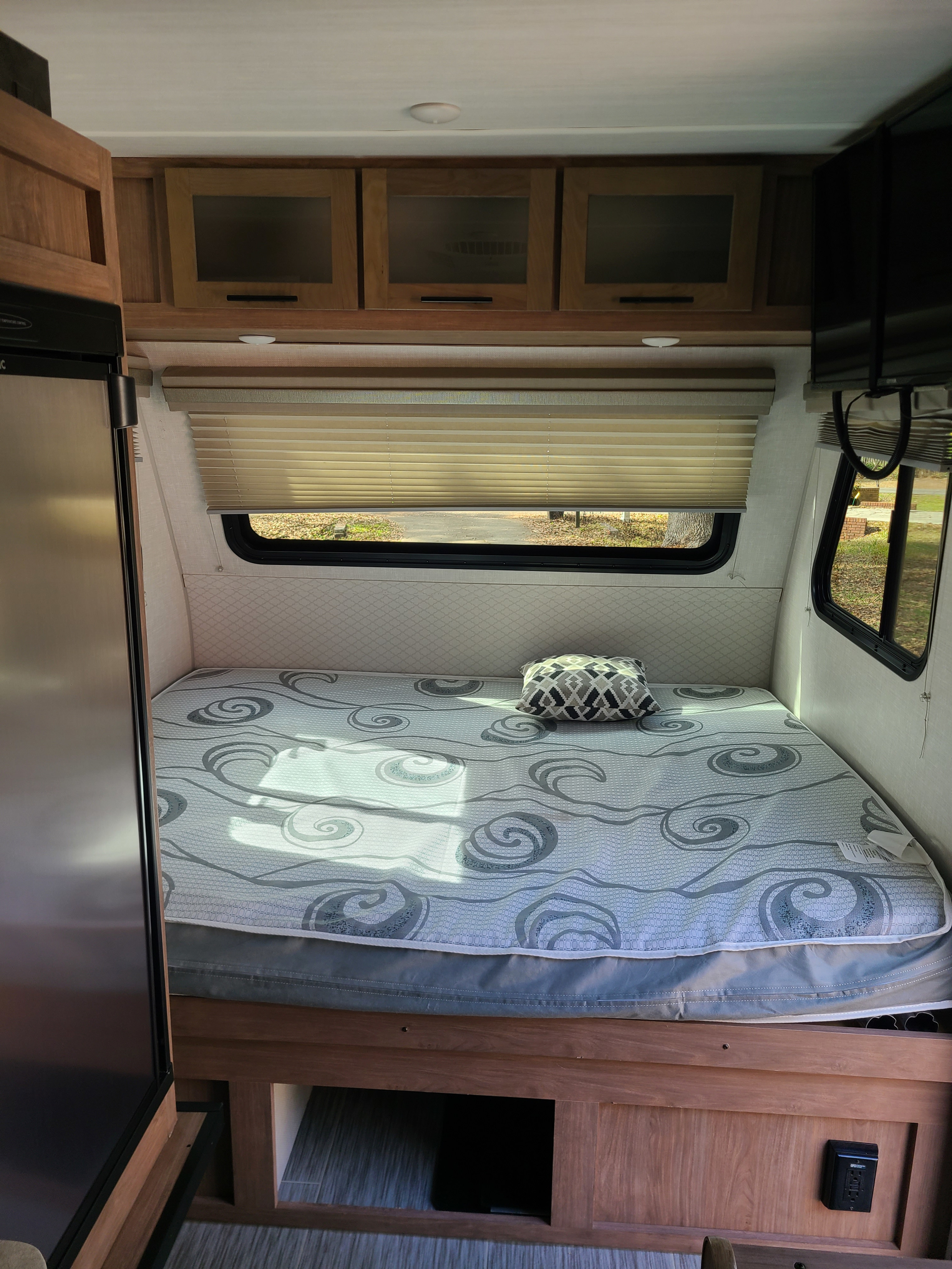 RV rental: a cozy sleeping area featuring a patterned bed, wood cabinets, and wide window with blinds.. No Boundaries 16 2021