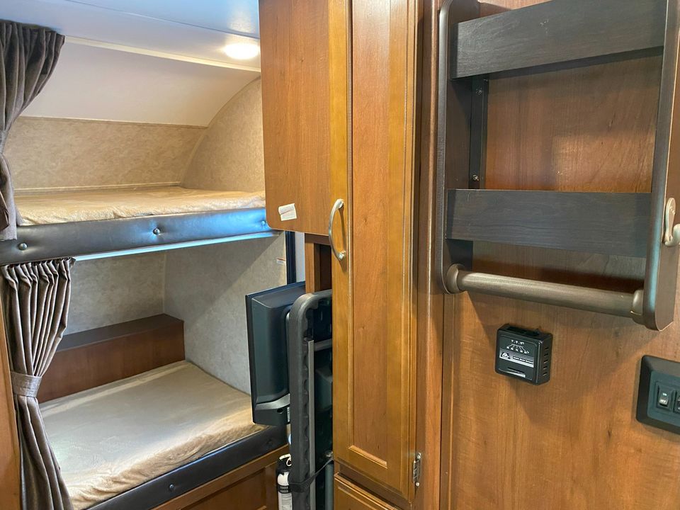 Inside an RV rental: view of comfortable bunk beds with curtains, wooden cabinetry, and wall-mounted amenities.. Jayco Hummingbird 2017