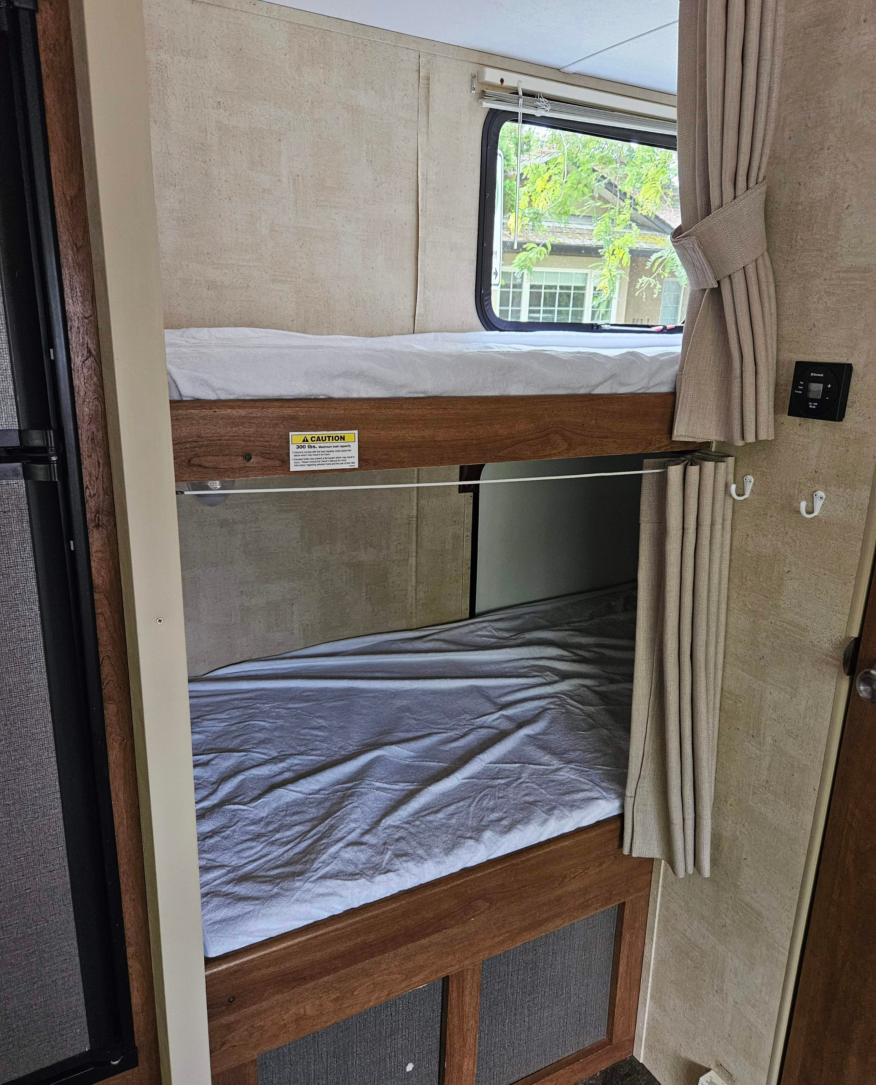 Inside an RV rental: two neatly made bunk beds with a window view, ideal for family travel and compact living.. Keystone RV Springdale 2014