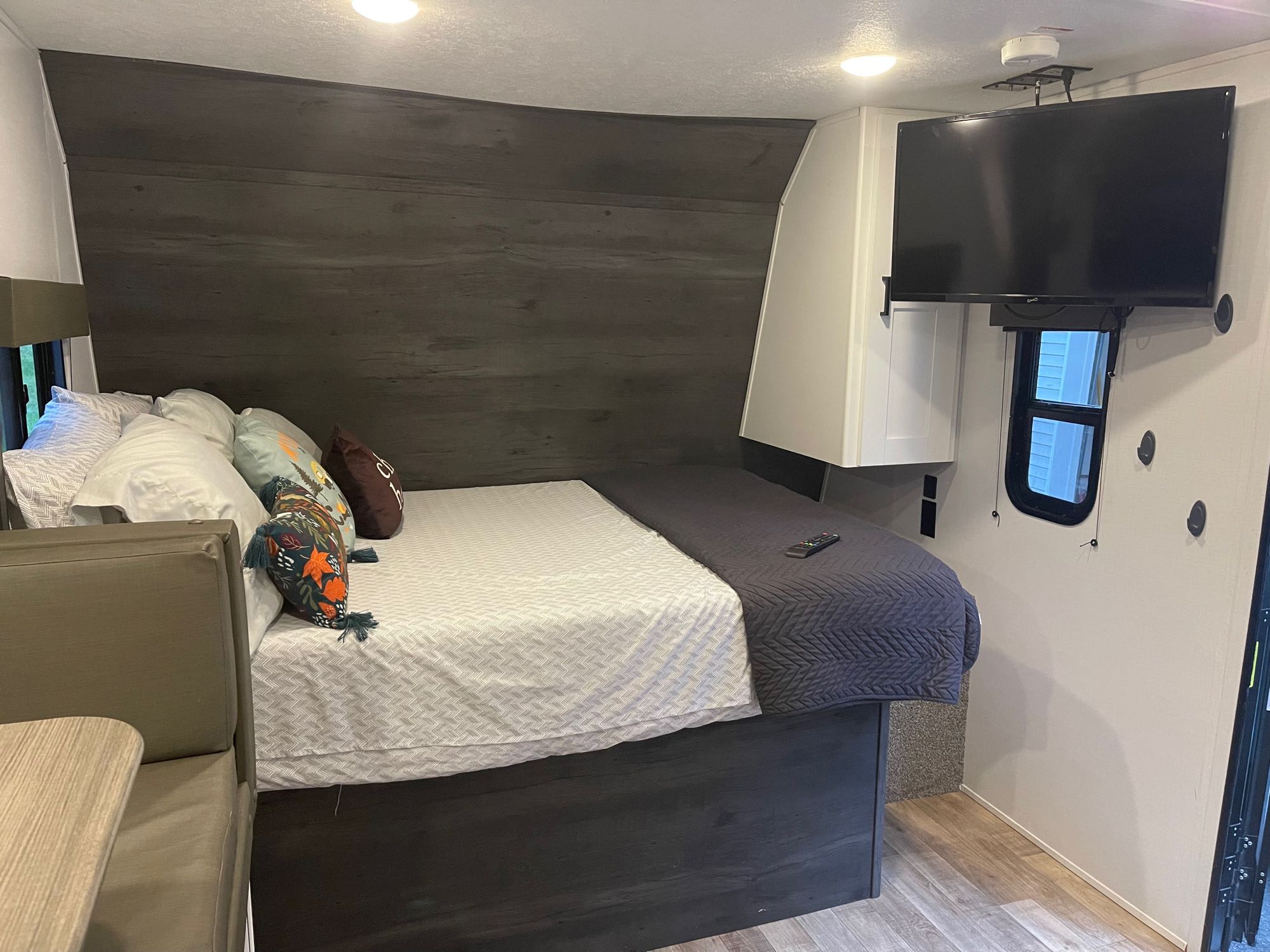 RV rental: A compact bedroom interior featuring a large bed with pillows, dark wood paneling, a wall-mounted TV, and a dinette.. Keystone RV Hideout 2021