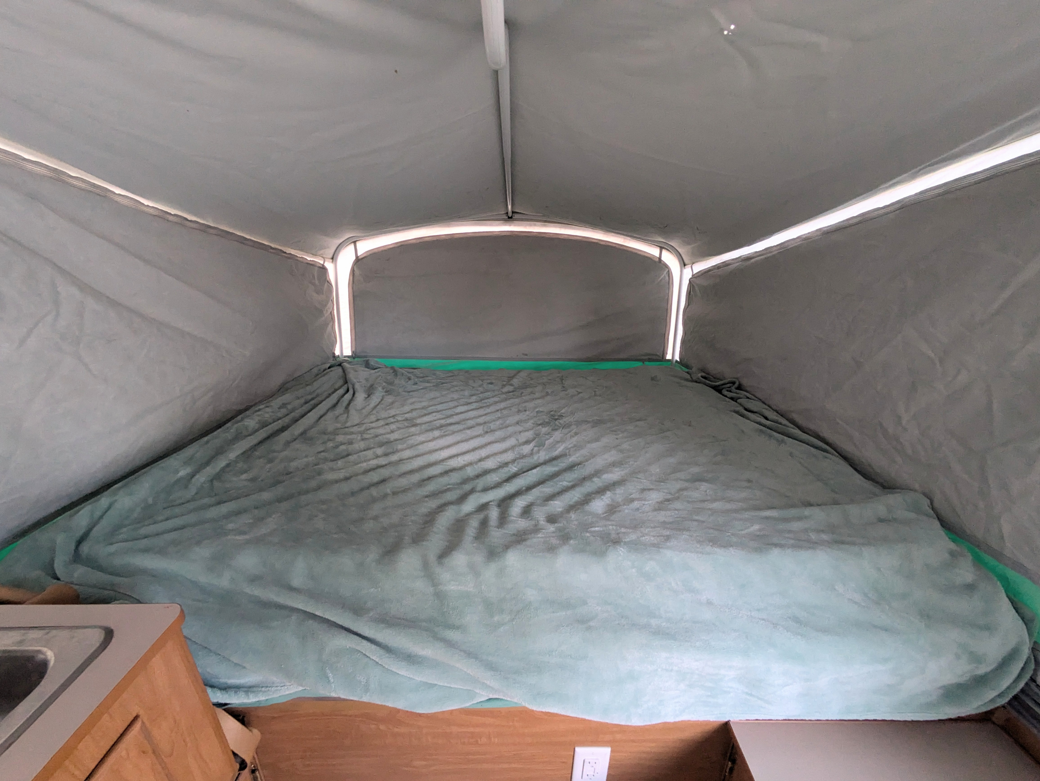 Inside an RV rental pop-up camper, featuring a spacious sleeping area with a soft blanket and bright canvas walls.. Fleetwood Sedona 2004