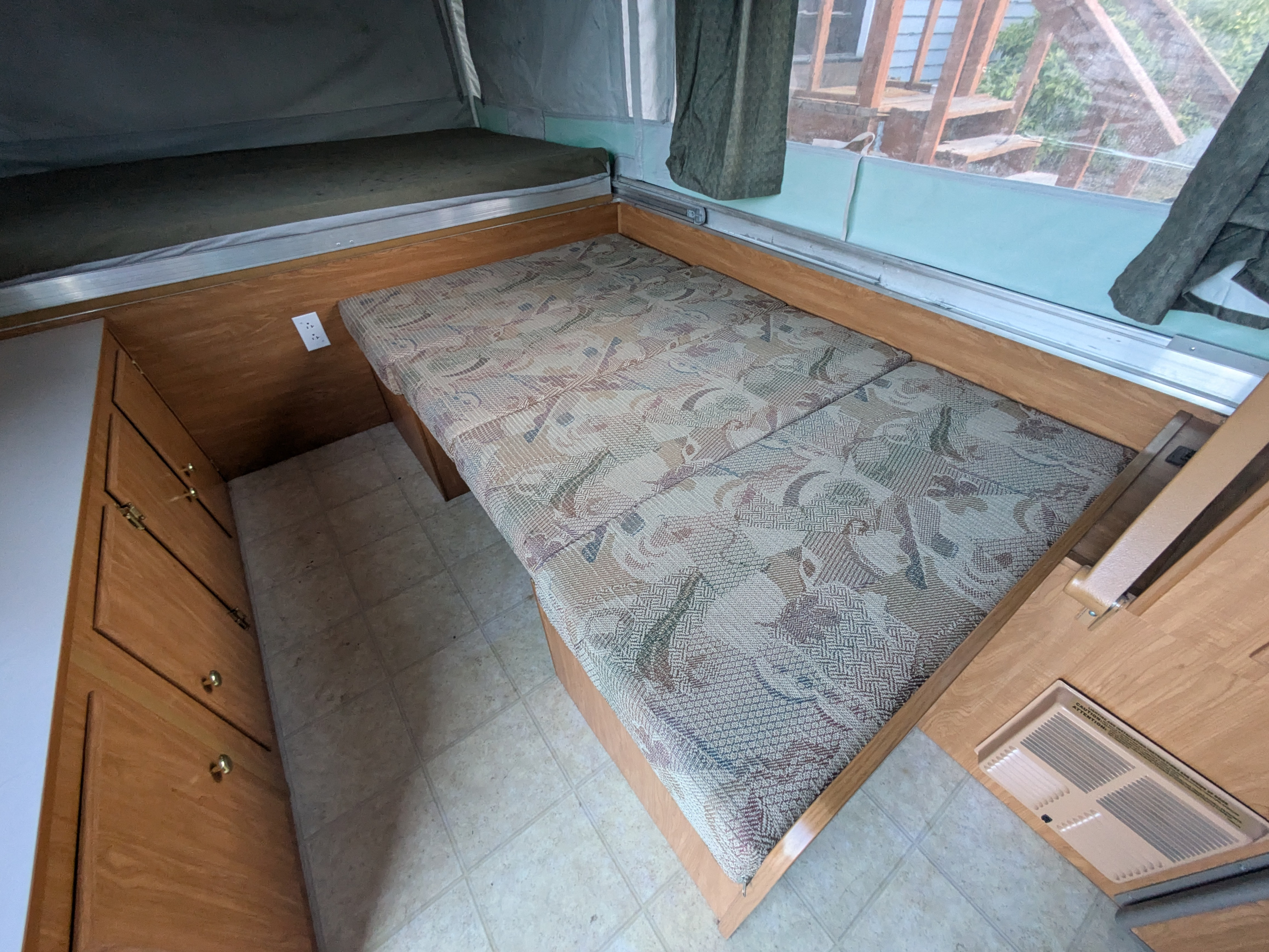 Inside a pop-up RV rental: compact living area with patterned cushions, bunk bed, cabinet, and vent.. Fleetwood Sedona 2004