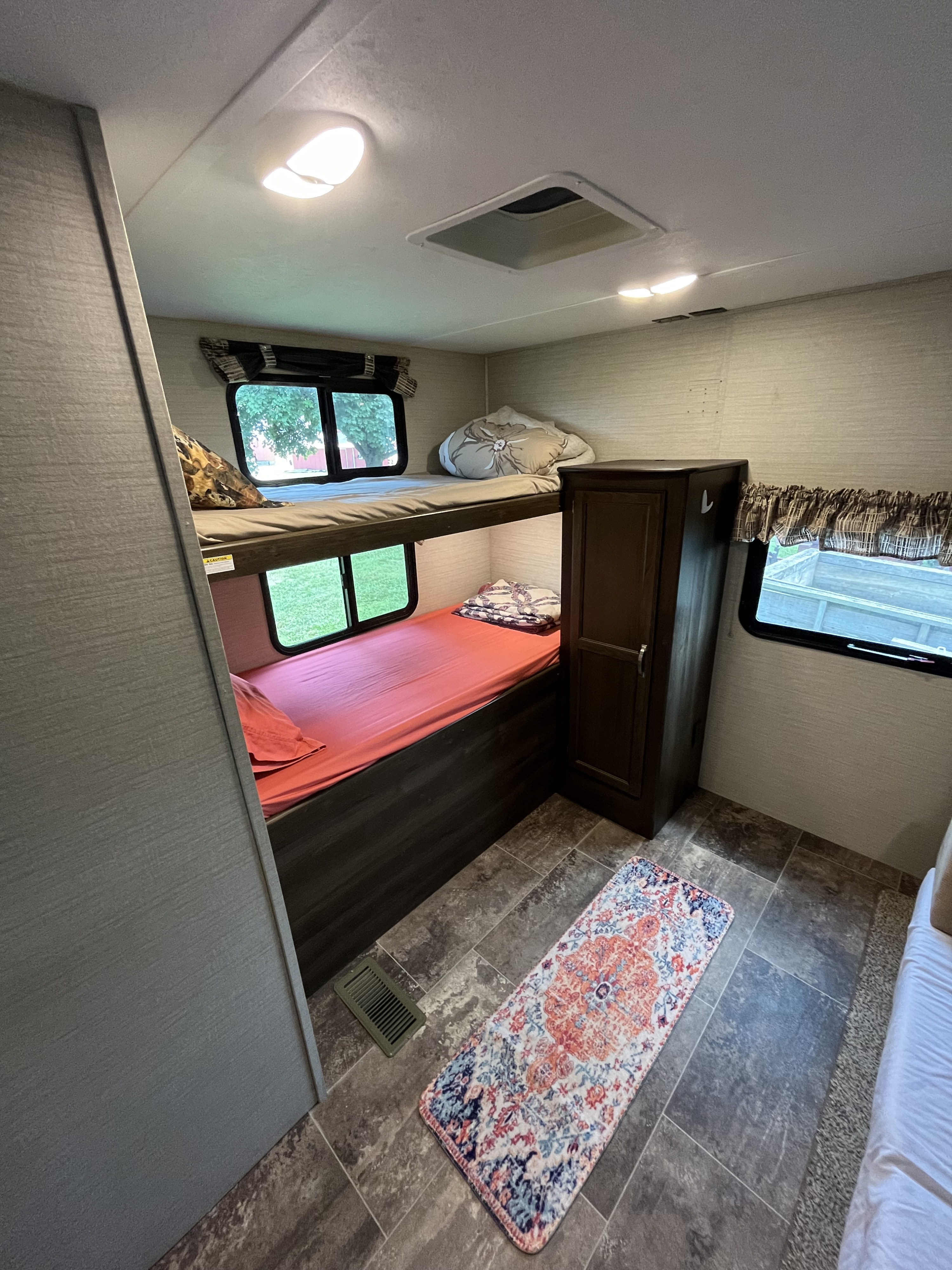 Cozy RV rental interior with bunk beds, windows, and a colorful rug on tile flooring.. Keystone RV Bullet Ultra Lite 2019