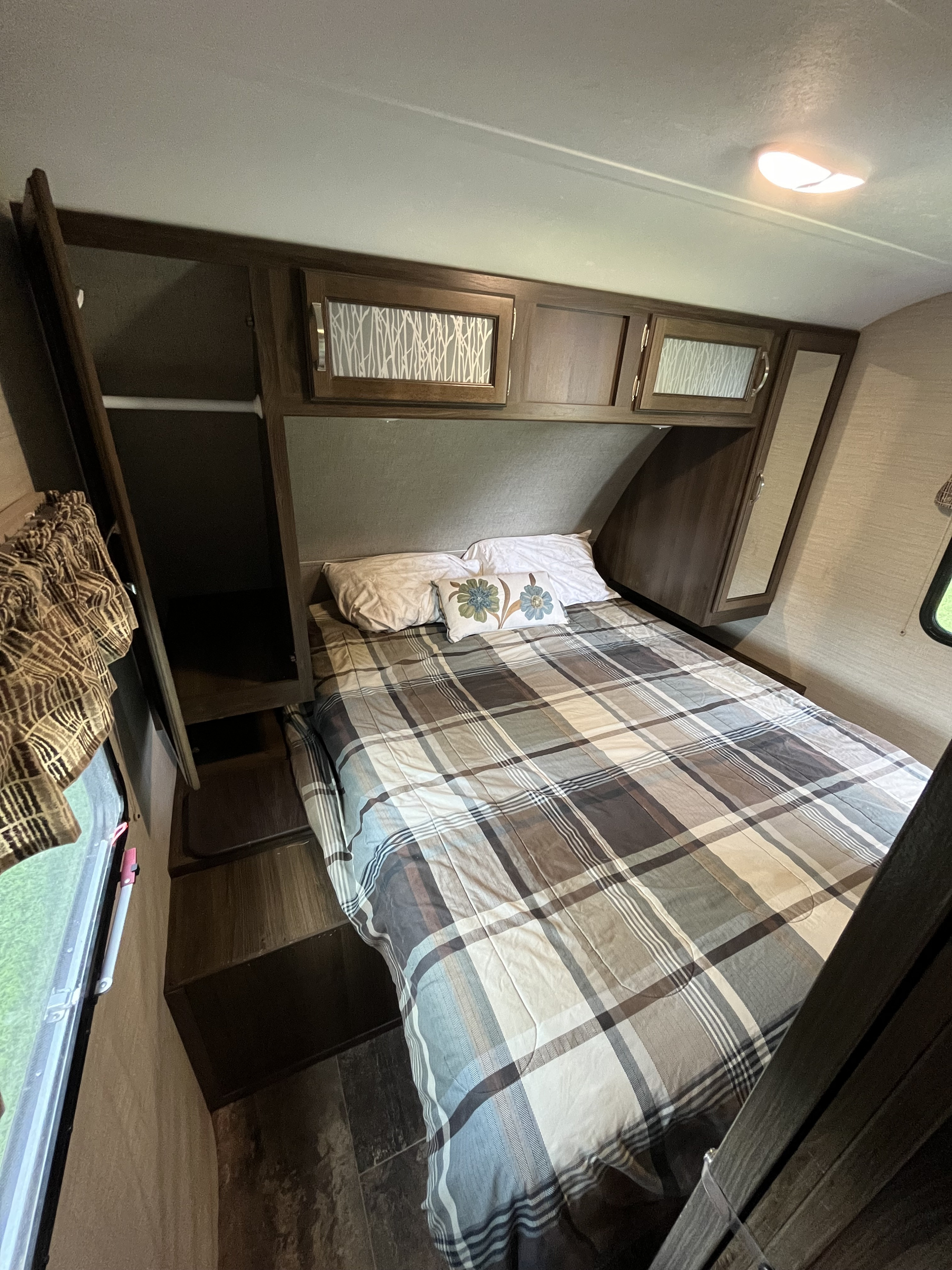 RV rental bedroom: a compact sleeping space featuring a plaid bed, pillows, overhead cabinets, and a side closet.. Keystone RV Bullet Ultra Lite 2019