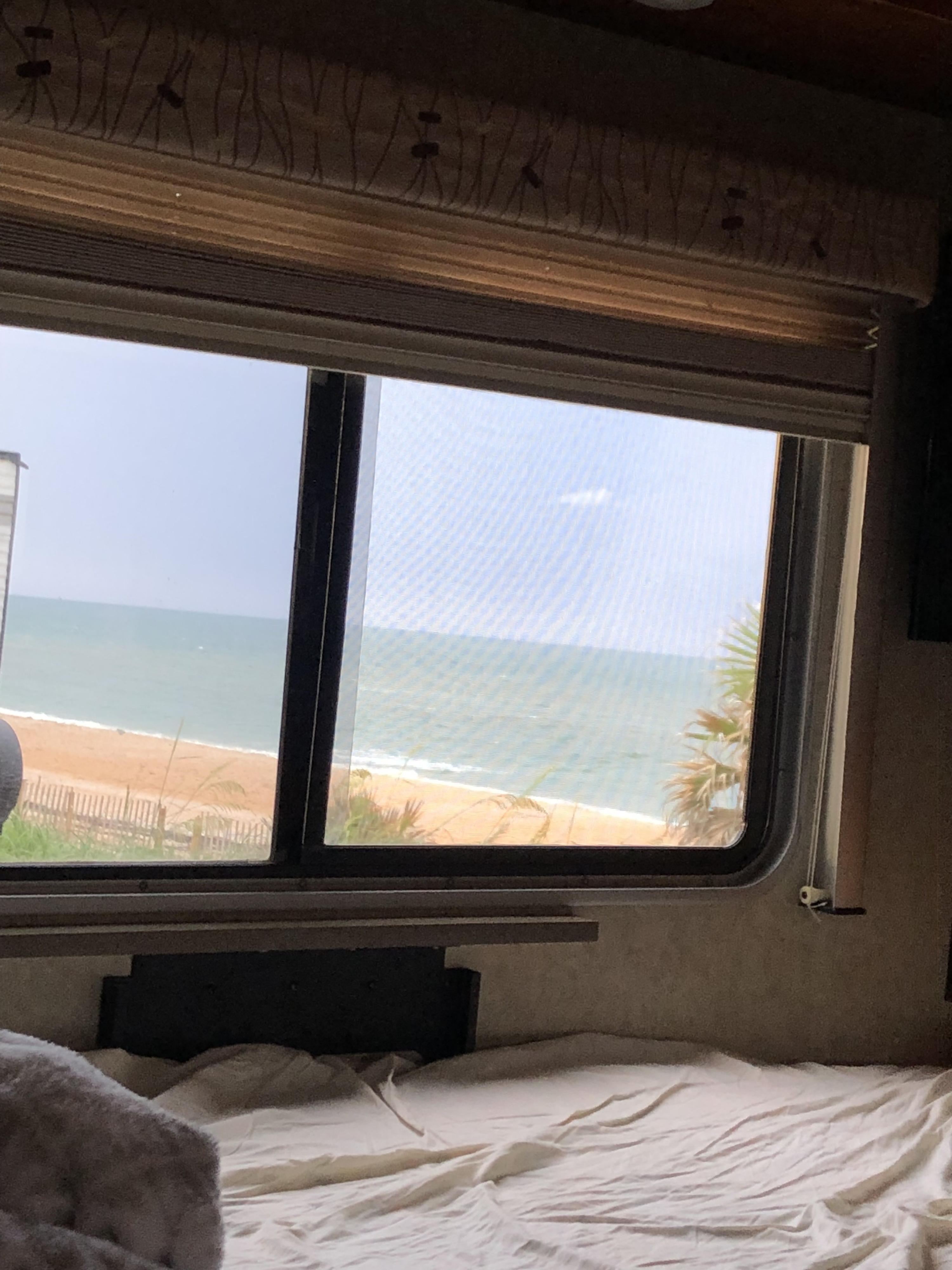 Interior of an RV rental bedroom with a window offering a serene beach and ocean view.. Pulse Pulse Motorhome 2009