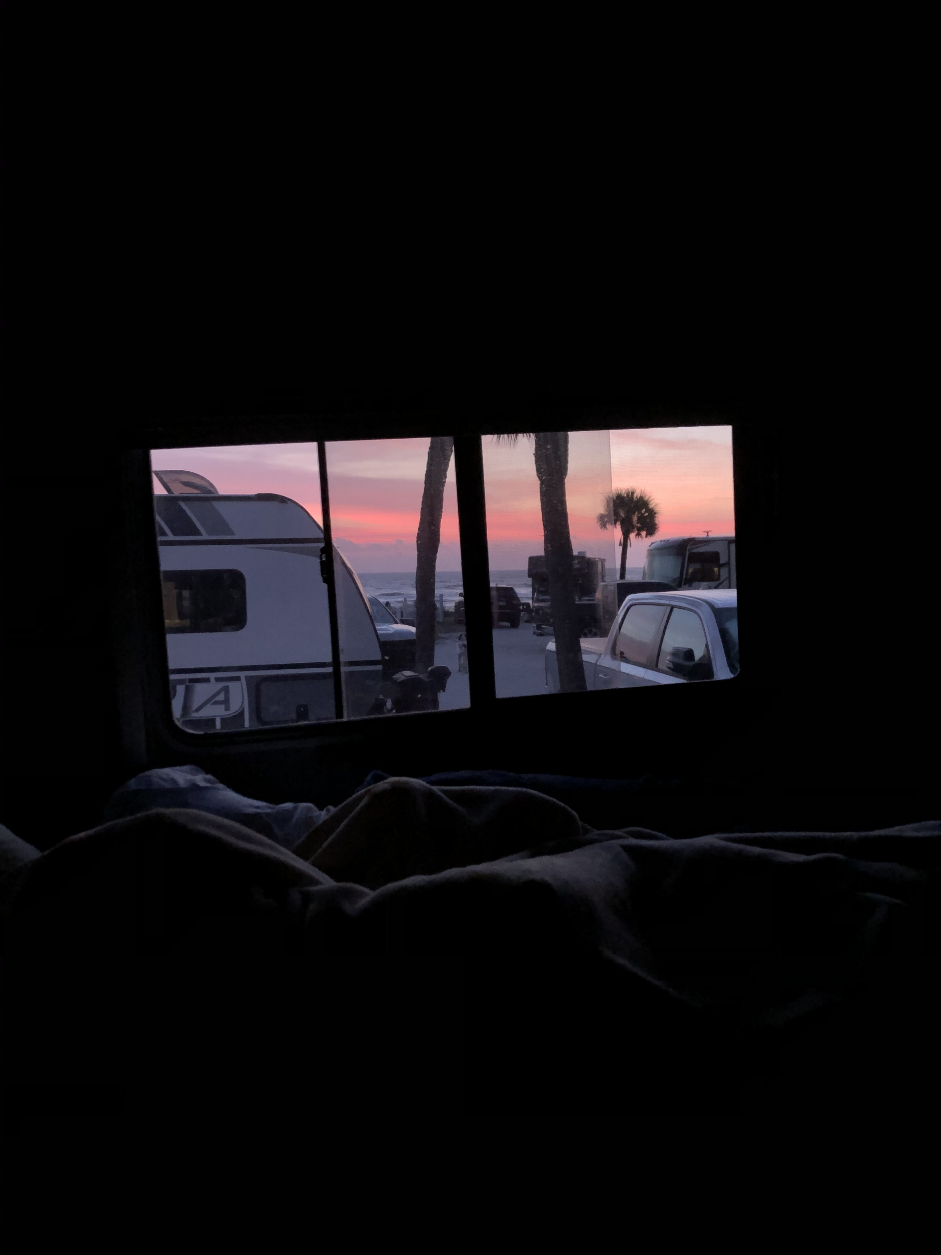 RV rental view: A stunning pink and orange sunset over the ocean, with palm trees and other vehicles visible from inside a cozy, dark interior.. Pulse Pulse Motorhome 2009