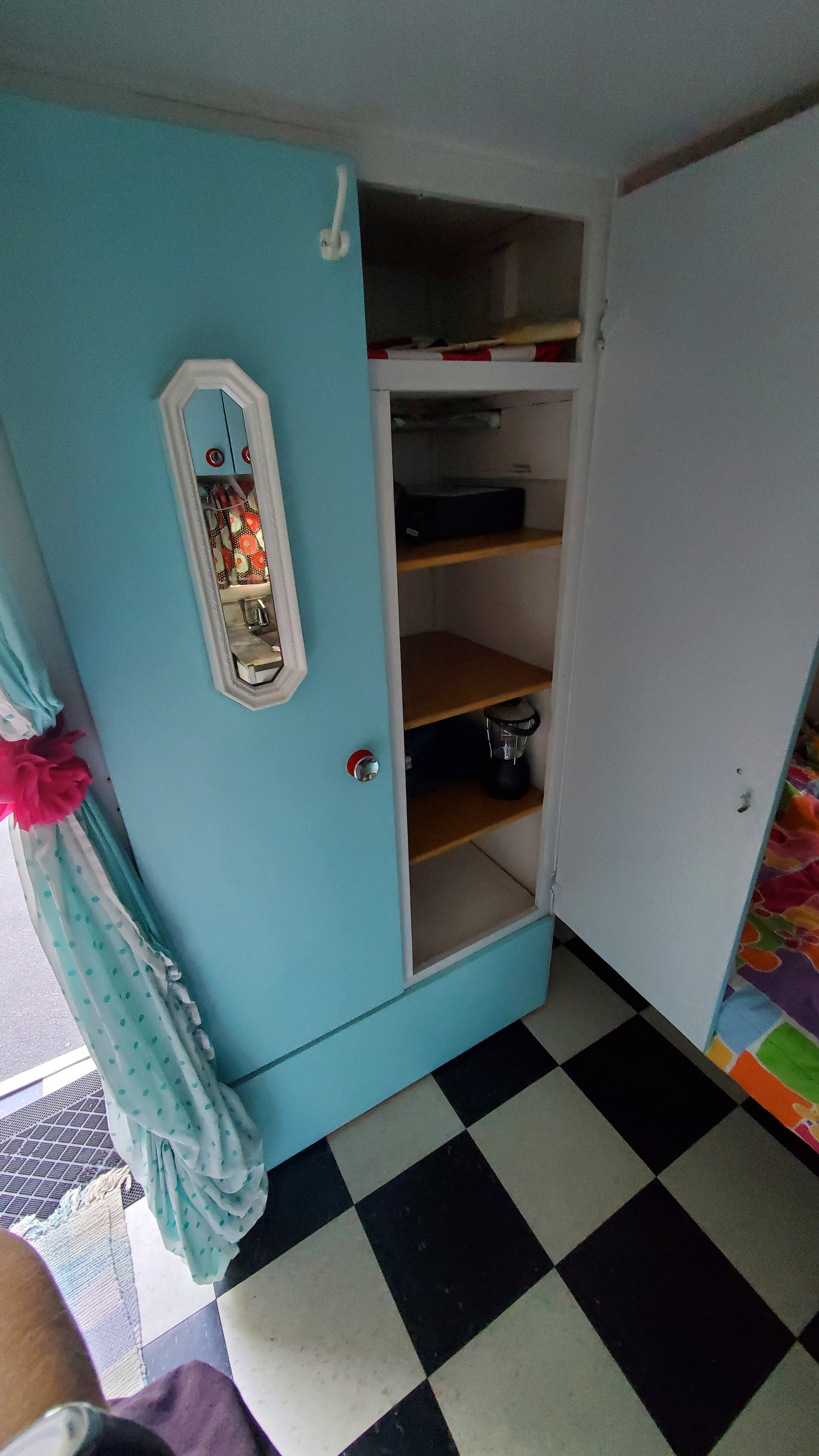 Vibrant RV rental interior: teal cabinet with mirror, organized shelves, and retro checkered flooring.. Skyline Layton 1968
