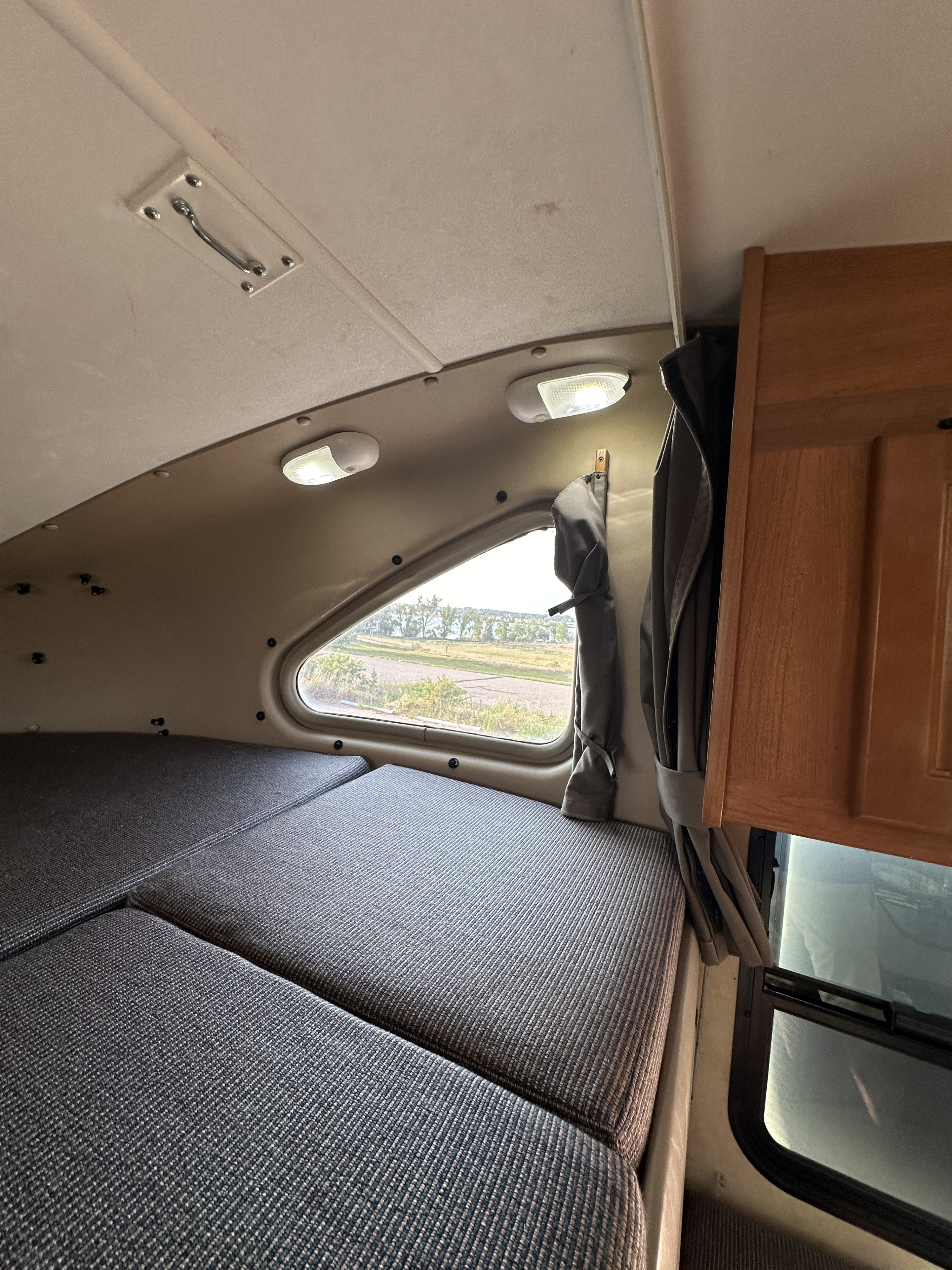 Cozy RV rental interior with a comfortable bed/seating area, a large window revealing a scenic outdoor view, and practical overhead lights.. Thor Majestic 2013