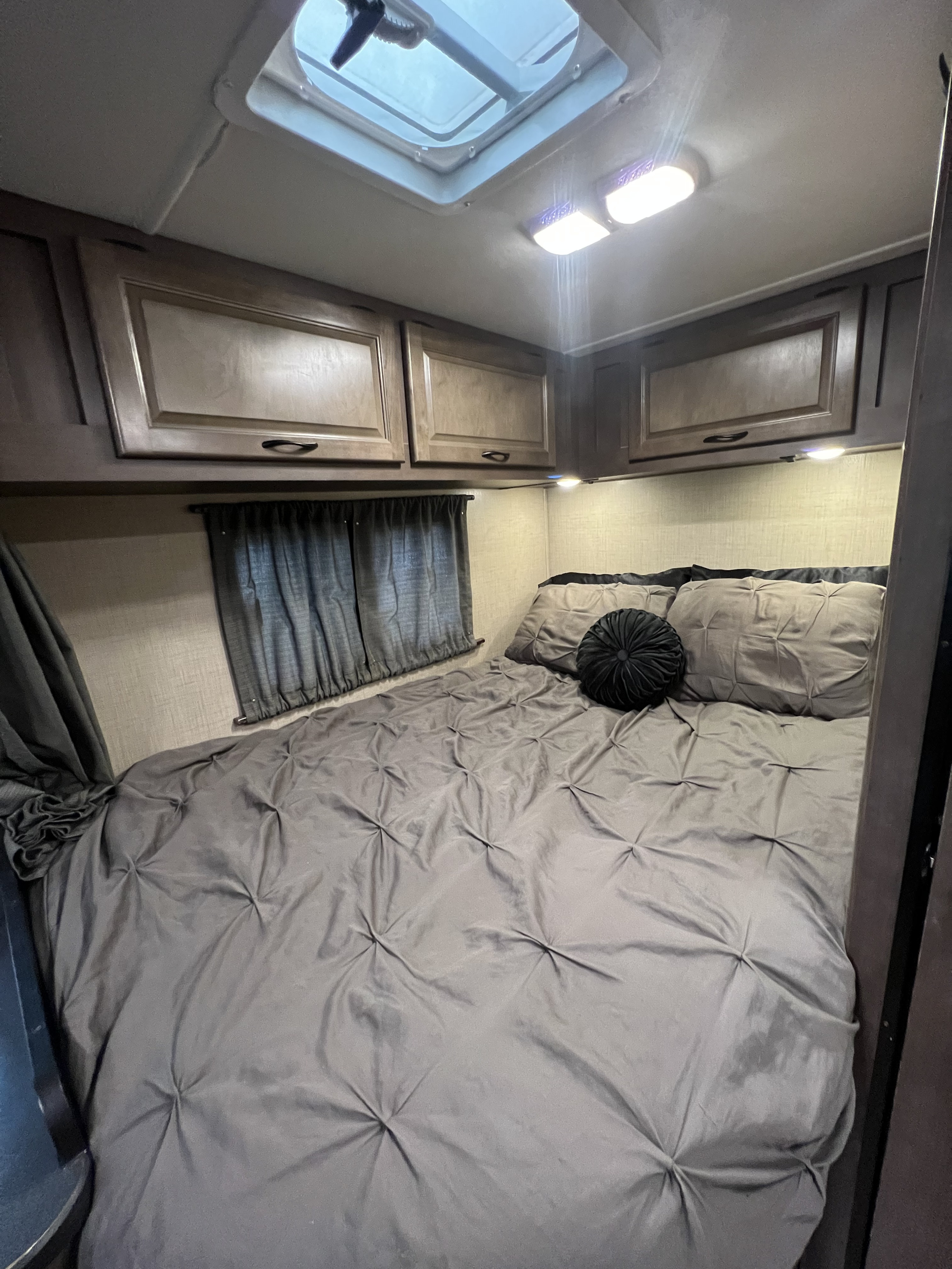 Cozy RV rental bedroom with gray bedding, overhead cabinets, and a skylight for natural light.. Thor Majestic 2018