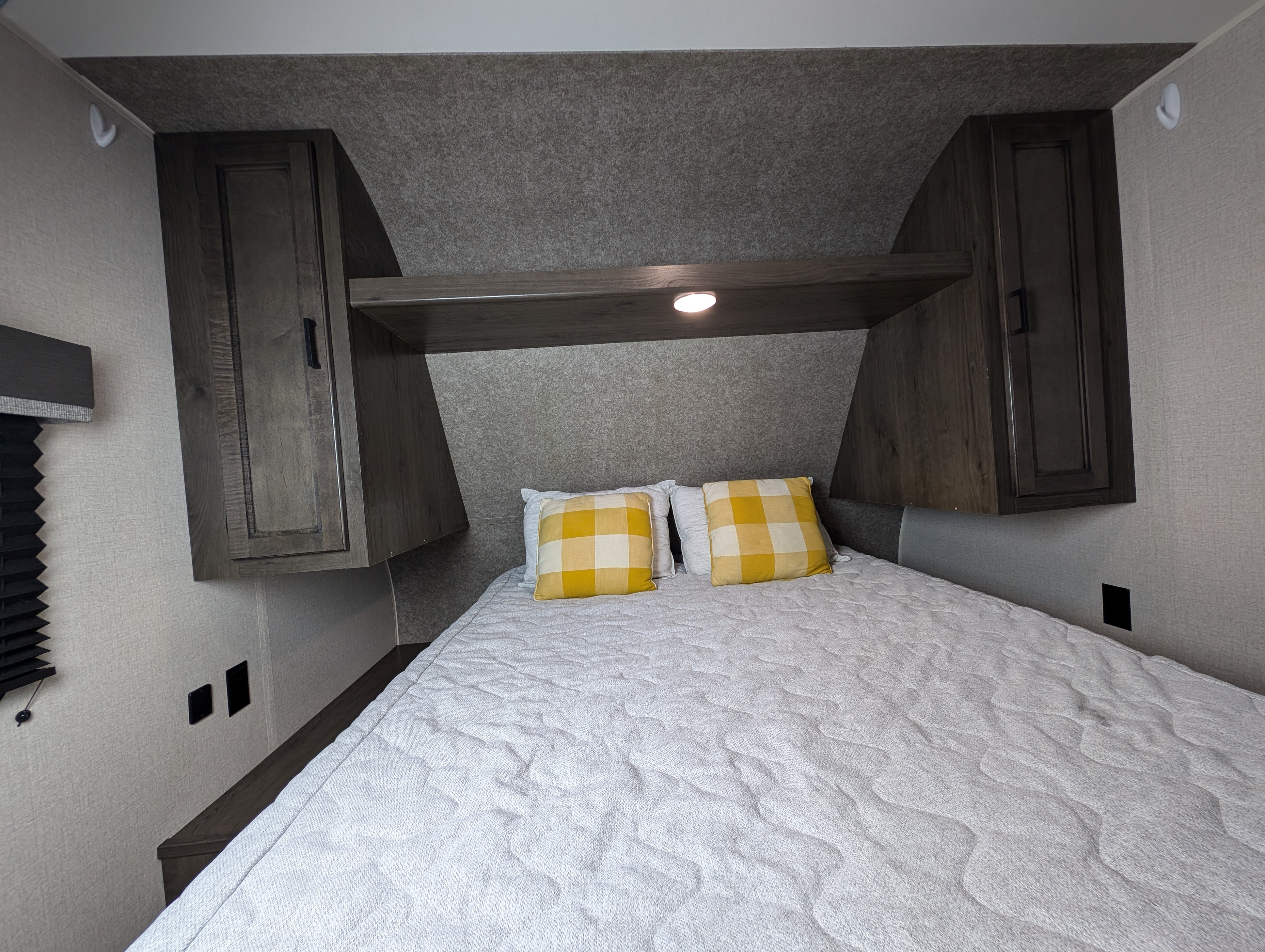 Cozy RV rental bedroom featuring a bed, yellow plaid pillows, overhead storage, and task lighting.. Starcraft Autumn Ridge 2021