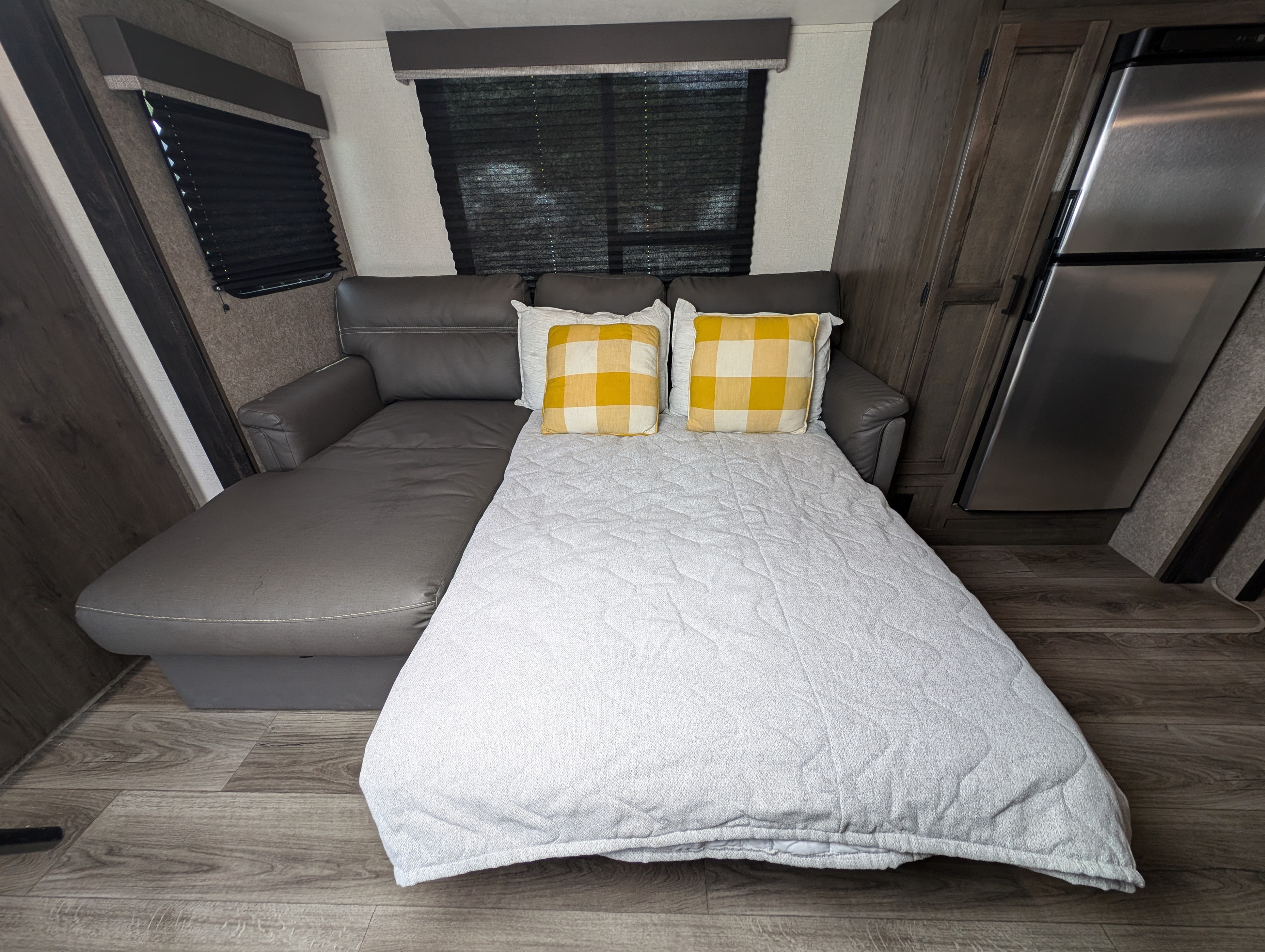 Cozy RV rental interior with a gray sofa bed, yellow plaid pillows, wood cabinetry, and a stainless steel fridge.. Starcraft Autumn Ridge 2021
