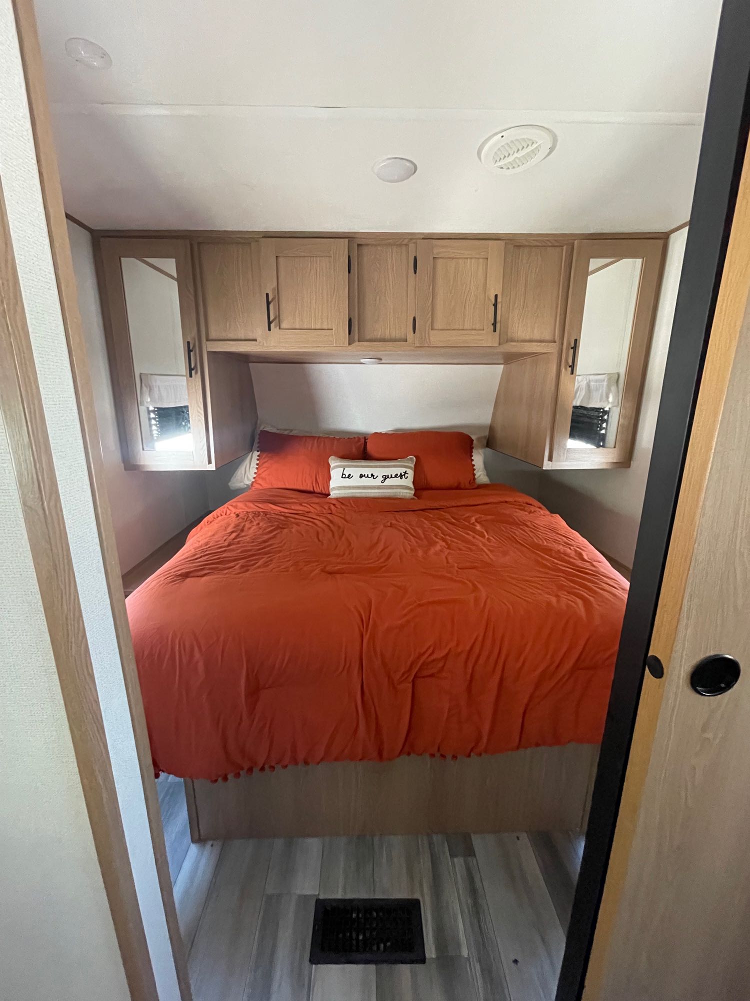 Cozy RV rental bedroom with an inviting orange queen bed, built-in overhead cabinets, and mirrored closets.. Forest River Avenger 27DBS 2022