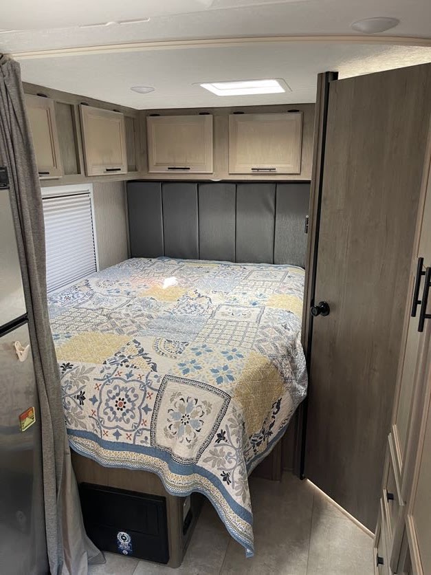 RV rental bedroom featuring a patterned bedspread, overhead cabinets, and a window. Perfect for travel.. Forest River Coachmen Crosstrail 2023