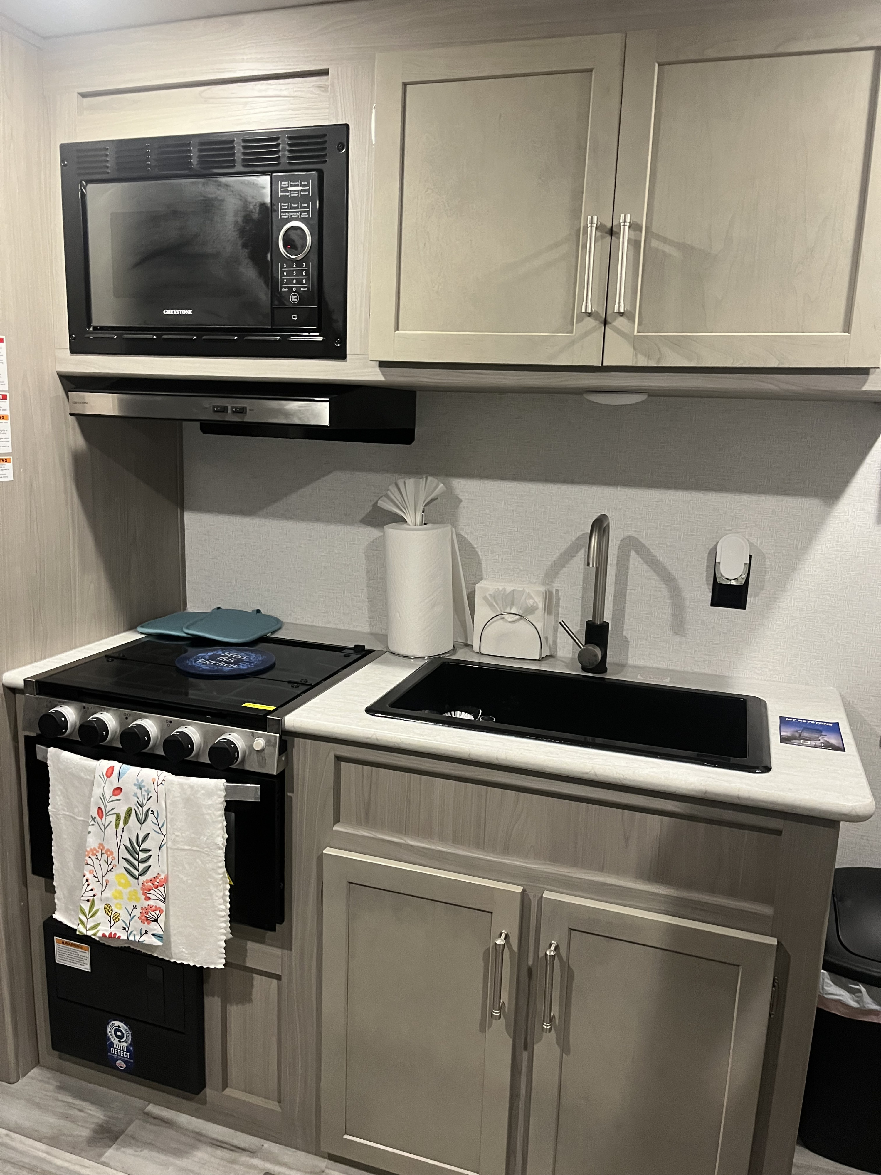 Compact RV rental kitchen with microwave, stove, and sink. Light cabinets provide organized storage in this functional space.. Keystone RV Springdale 2024