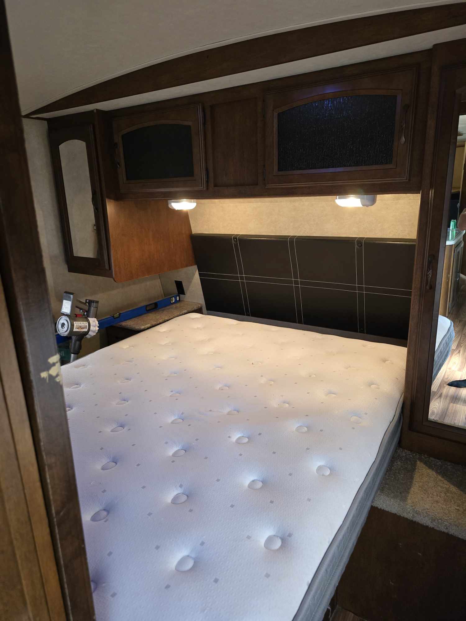 Inside a cozy RV rental bedroom: clean mattress, dark headboard, and wood cabinets. Ready for your next adventure!. Forest River Wildwood Heritage Glen Lite 2014