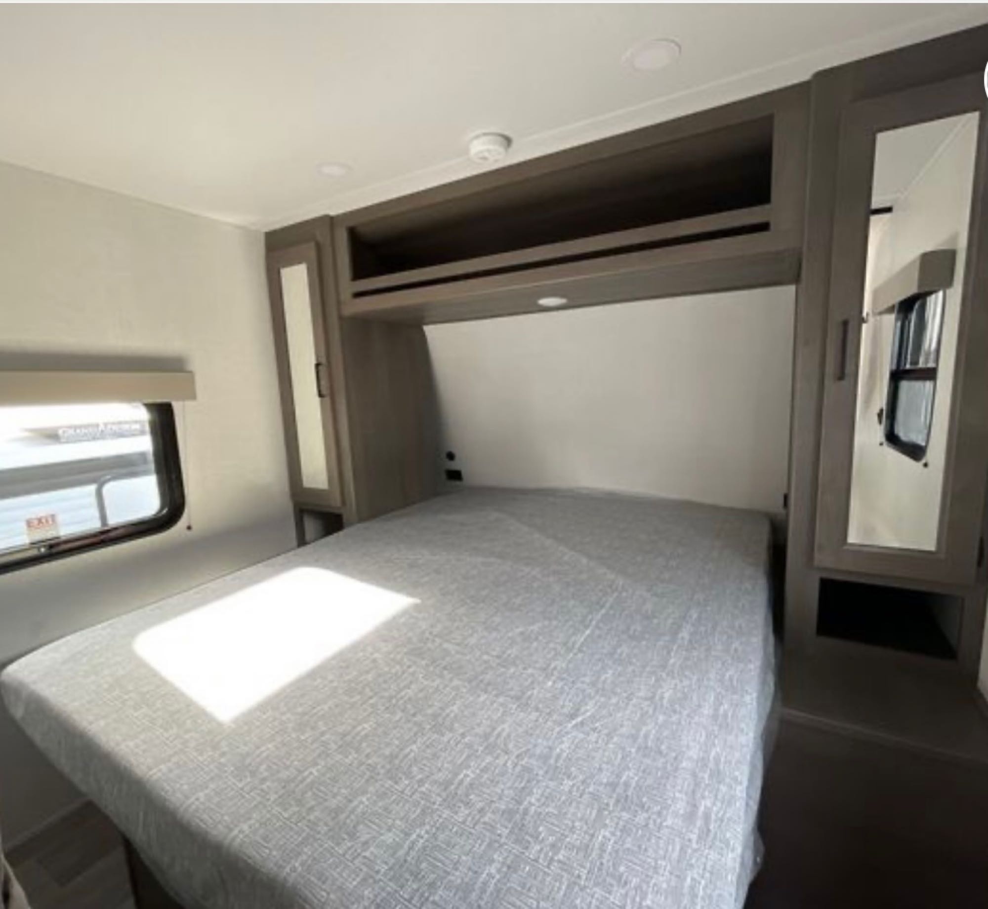 Bright, modern RV rental bedroom featuring a large bed, overhead storage, mirrored closets, and a window. Ideal for travel.. Grand Design Transcend Xplor 2024