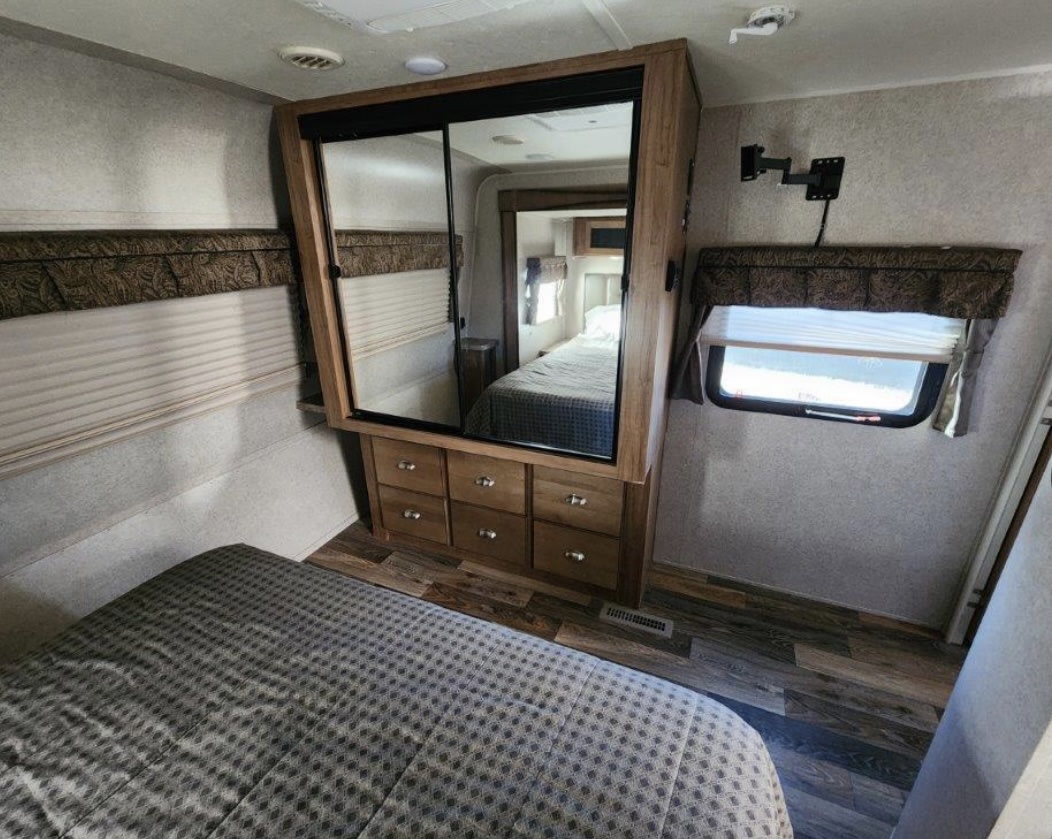 Cozy RV rental bedroom features a bed, mirrored closet with drawers, and a window, ideal for comfortable travel.. Forest River Rockwood Signature Ultra Lite 2017